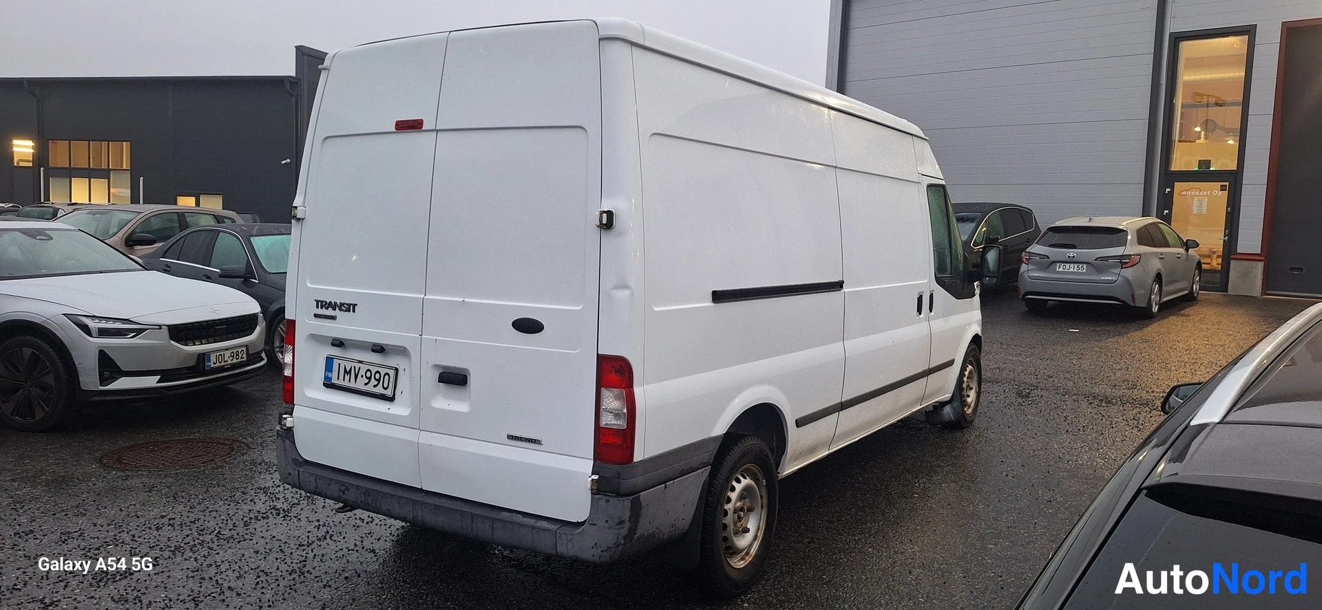 Takaviisto: Valkoinen Ford Transit -pakettiauto takaa ja oikealta sivulta; takaluukussa TRANSIT-teksti ja rekisterikilpi.