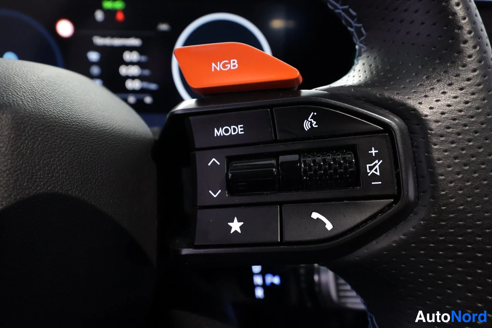 Ohjaamo: Close-up of the right side of a perforated leather steering wheel showing mode selection buttons and an orange drive mode selector labeled NGB