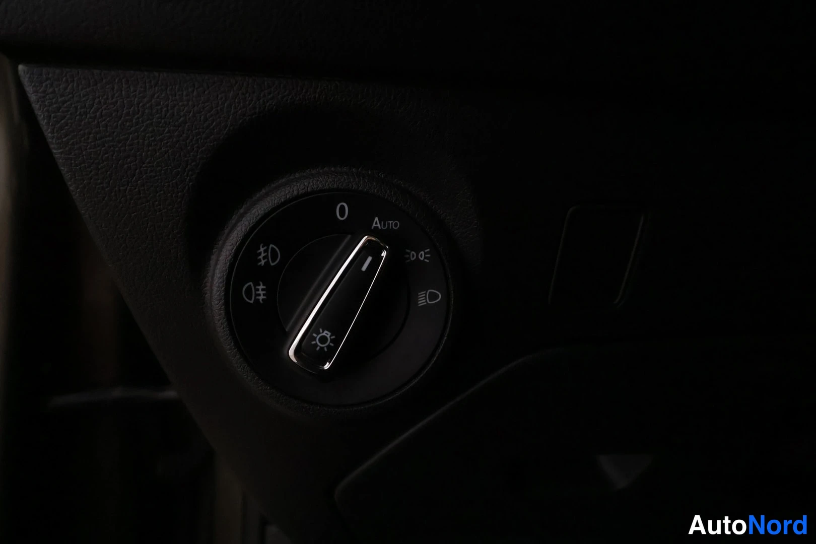 Muu: Sisätilakuva ajovalojen kytkimestä kojelaudassa, jossa Auto-asento ja valosymbolit näkyvät.