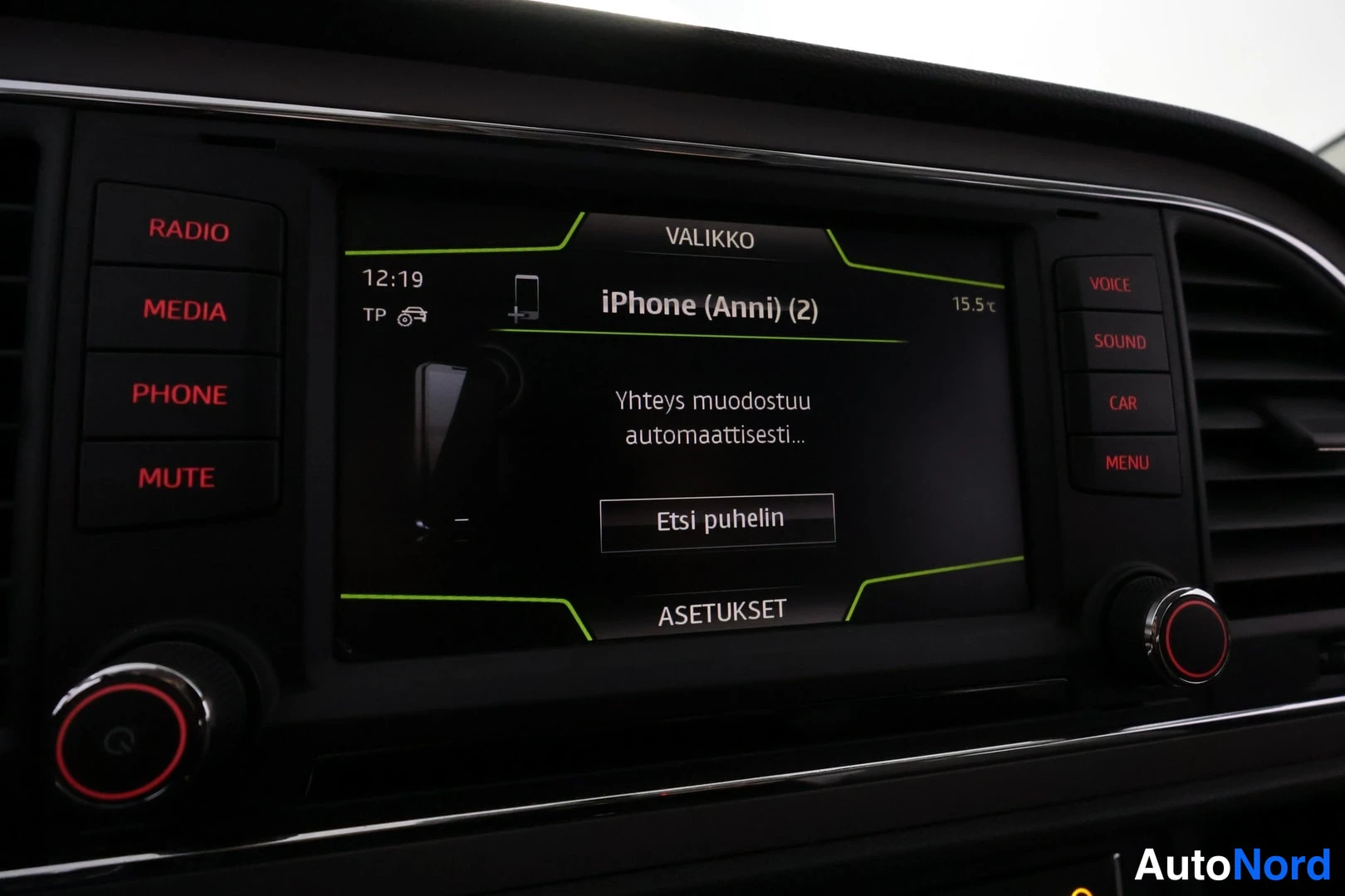 Yksityiskohta: Infotainment-näytön puhelinvalikko: 'iPhone (Anni) (2)', teksti 'Yhteys muodostuu automaattisesti...' ja valinta 'Etsi puhelin'.