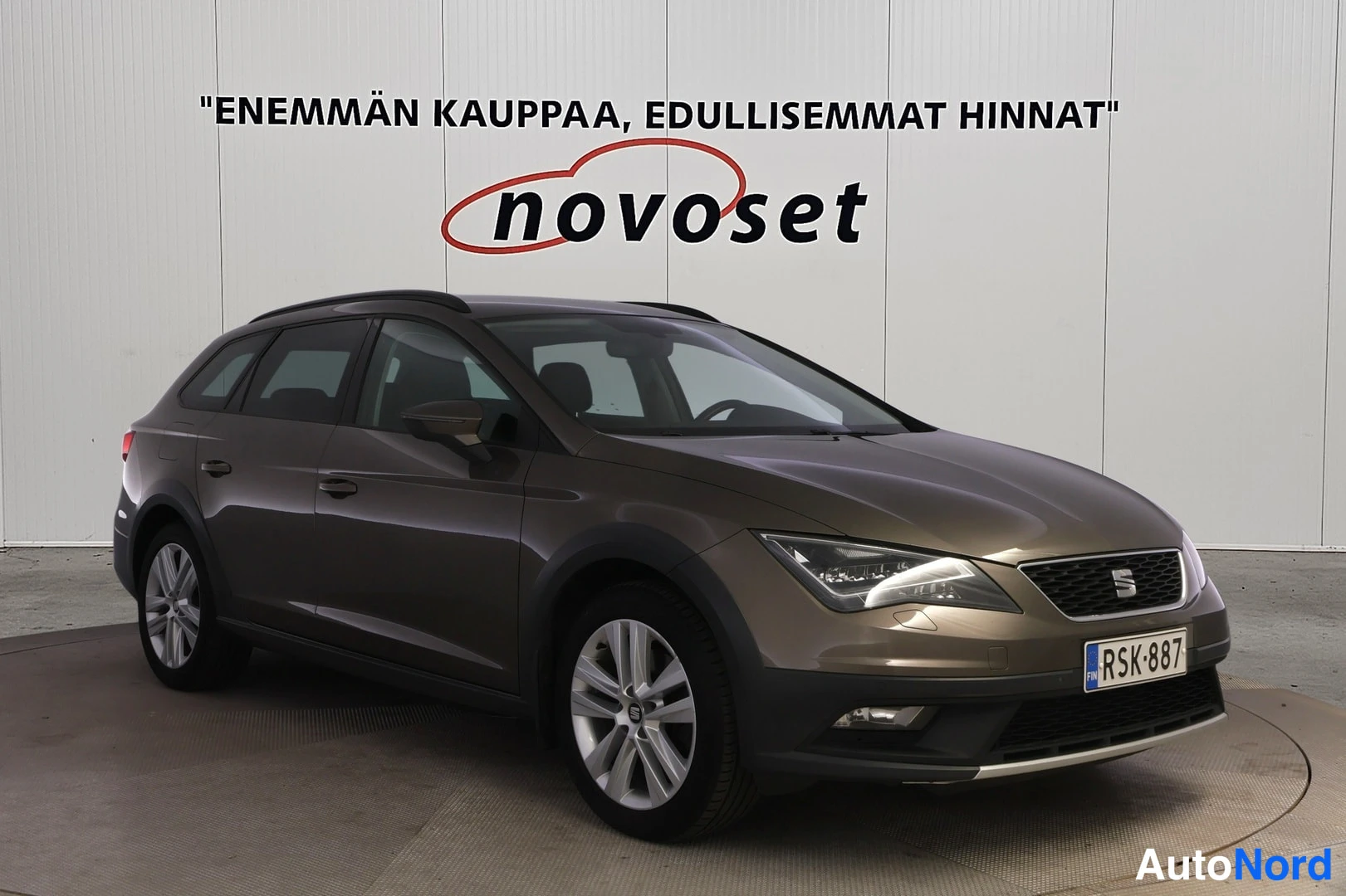 Etuviisto, nokka oikealle: Ruskean Seat Leon X-Perience -farmariauto kuvattu etuviistöstä hallissa, rekisterikilpi.