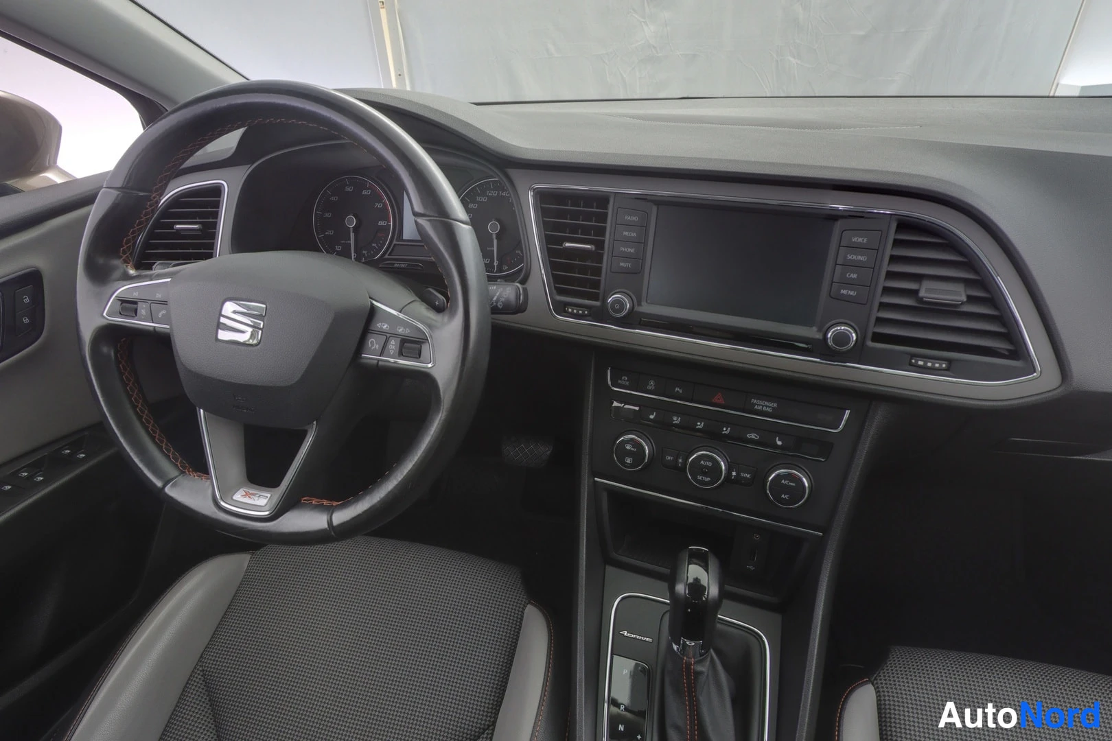 Muu: Seat-autoon sisätilat lähikuvana: ohjauspyörä Seat-merkillä, mittaristo ja keskinäyttö, automaattivaihteiston vaihdekeksi.