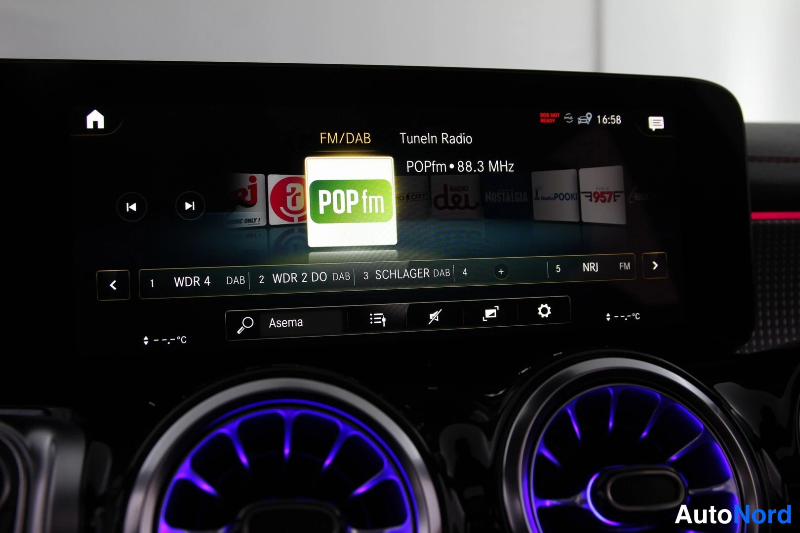 Yksityiskohta: Radionäytöllä FM/DAB ja TuneIn Radio, valittuna POPfm 88,3 MHz; asemalistassa WDR 4, WDR 2 DO, SCHLAGER DAB ja NRJ FM. Etualalla pyöreät ilmastointisuutimet sin