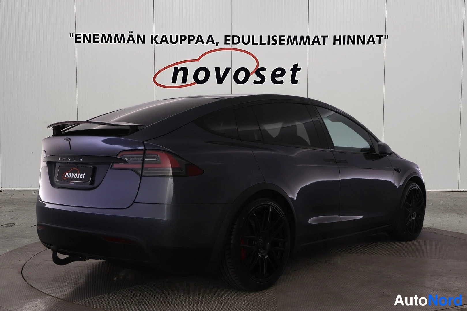 Takaviisto: Tesla Model X takaviisto vasemmalta, näkyvissäpunaiset jarrusatulat ja nuevoset-kyltti