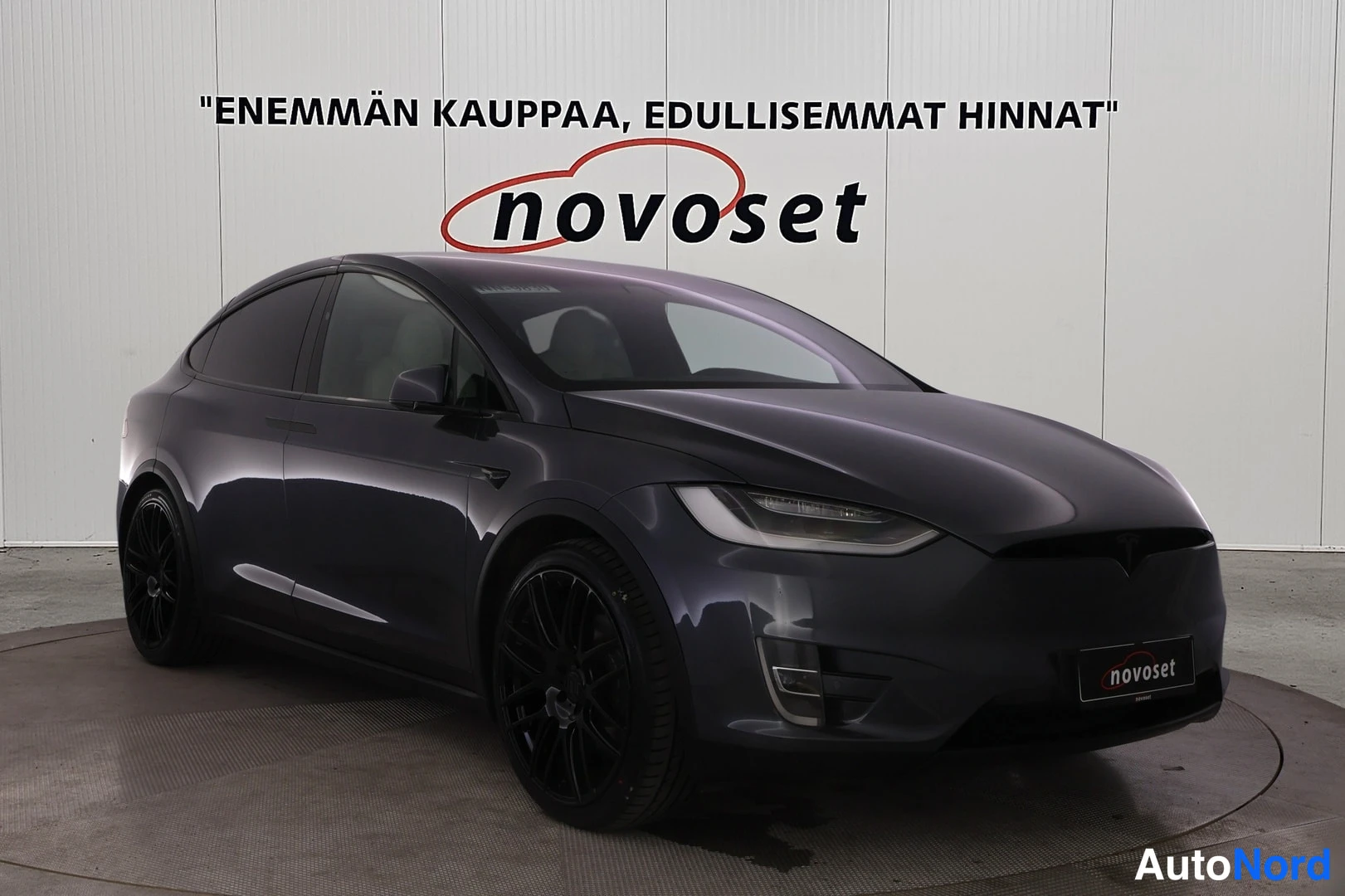 Etuviisto, nokka oikealle: Tummanharmaa Tesla Model X etuviistosta oikealta; keula ja molempien ovien sivupaneelit näkyvissä, mustat kevytmetallivanteet, vaalea studiovaaka taustal