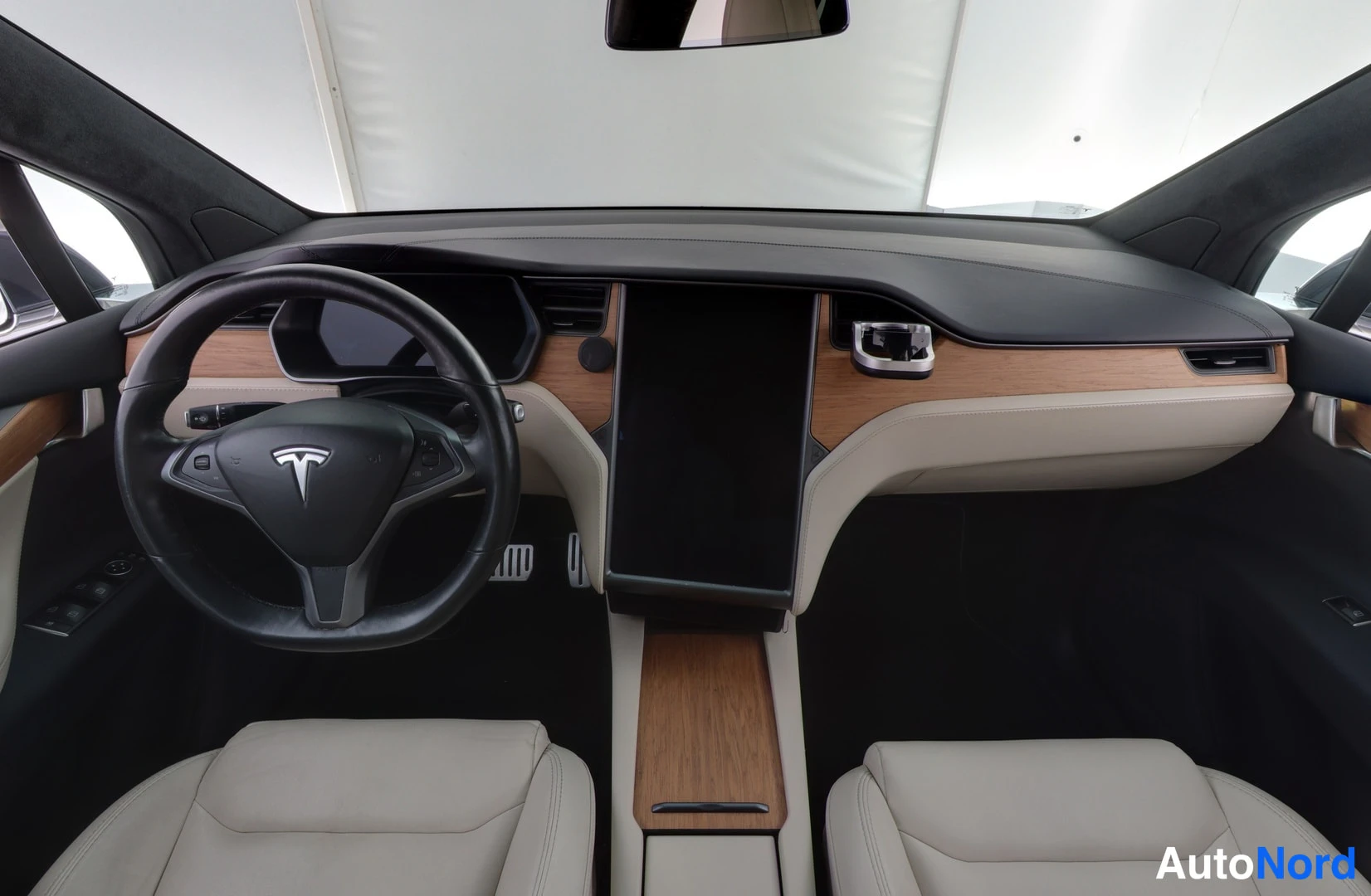 Muu: Teslaan sisustasta ylhäältä kuvattu näkymä: musta ohjauspyörä Tesla-logolla, suuri keskinäyttö, puukoristeet, beiget etuistuimet ja tumma kojelauta.