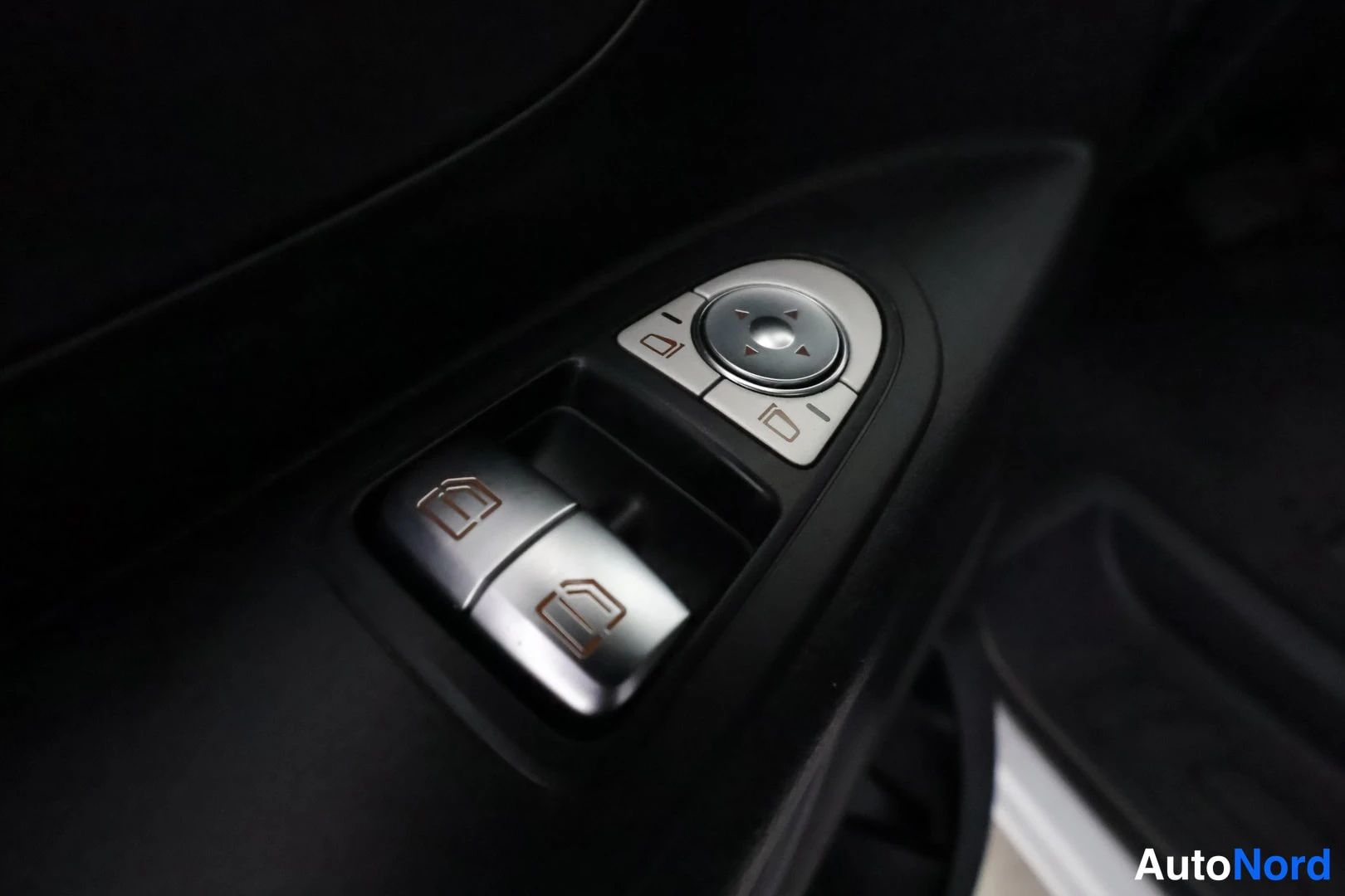 Ohjaamo: Close-up of the driver-side door panel showing a set of silver window switches and an electronic side-mirror adjustment dial with directional arrows.