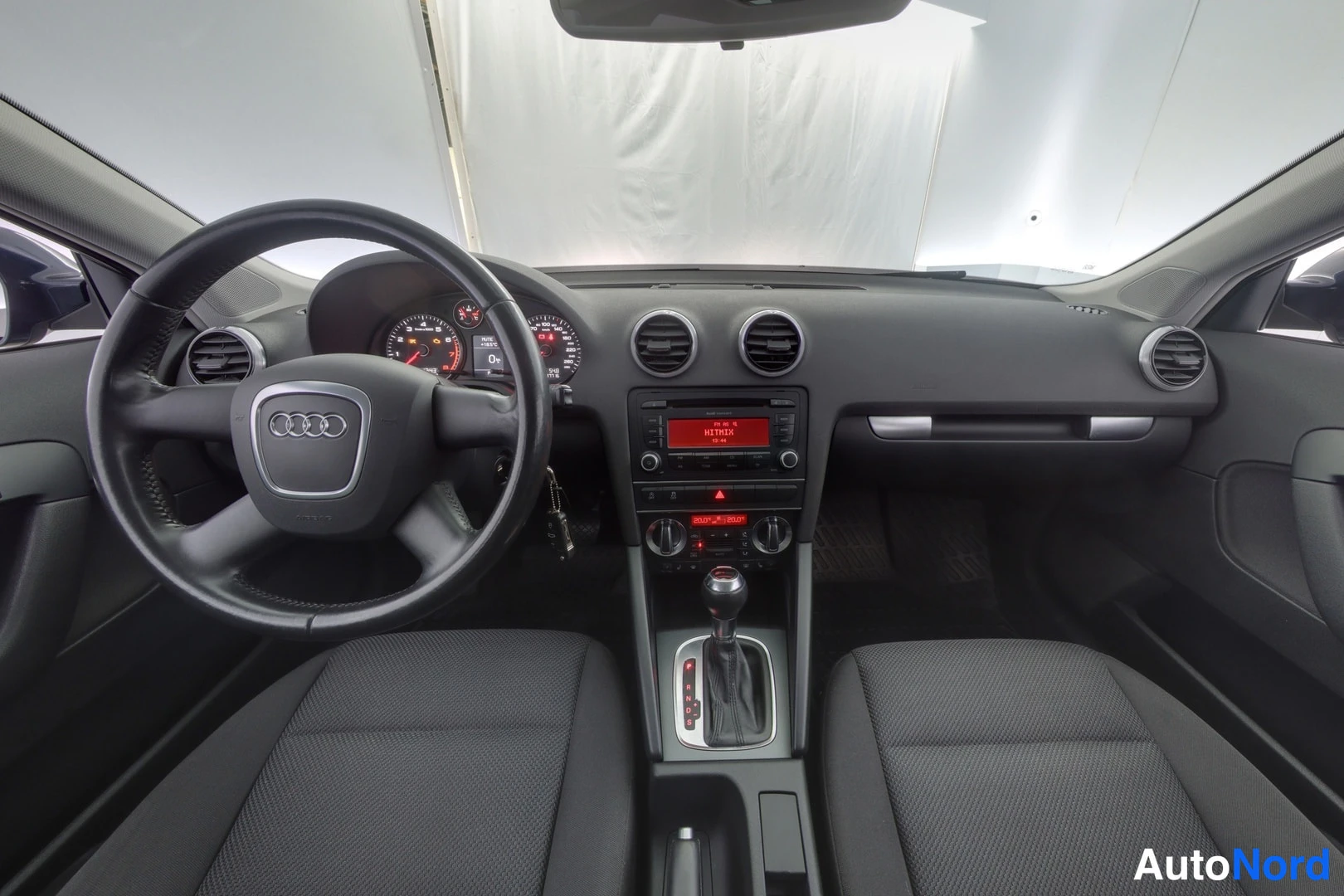 Muu: Audi A3:n ohjaamo nähtynä takaistuimelta: ohjauspyörä, mittaristo, radio ja automaattivaihteiston valitsin.