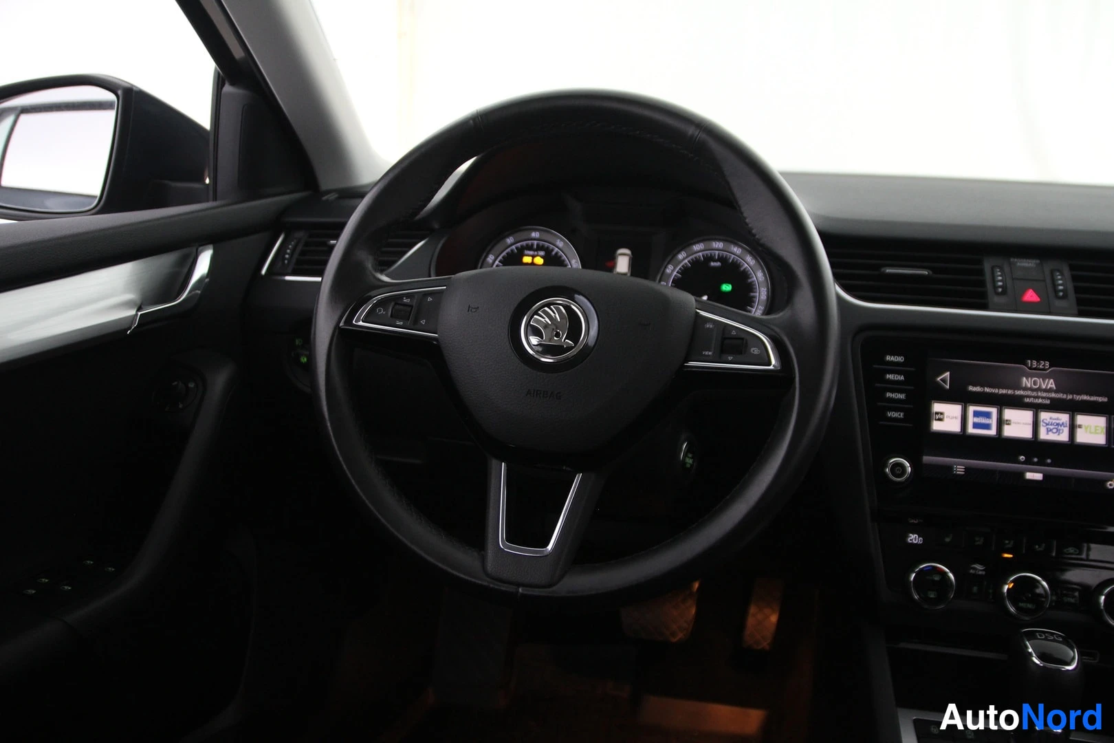 Muu: Ohjaamo etuovelta kuvattuna: Skoda-merkkinen ohjauspyörä, mittaristo ja kosketusnäyttö-radio, jonka näytöllä lukee NOVA.