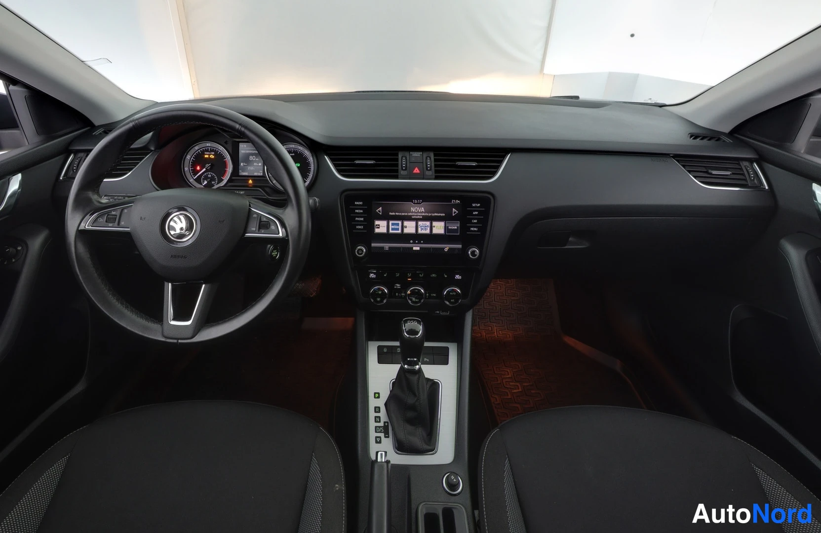 Sivulta: Kuljettajan näkymä auton sisällä: Skoda-ohjauspyörä, analogiset mittarit, kosketusnäyttöradio ja keskikonsolin automaattivalitsin.