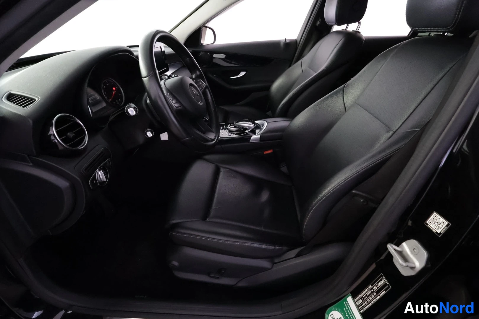 Ohjaamo: Side view of the driver's seat and cockpit area, displaying black leather upholstery and the center console.