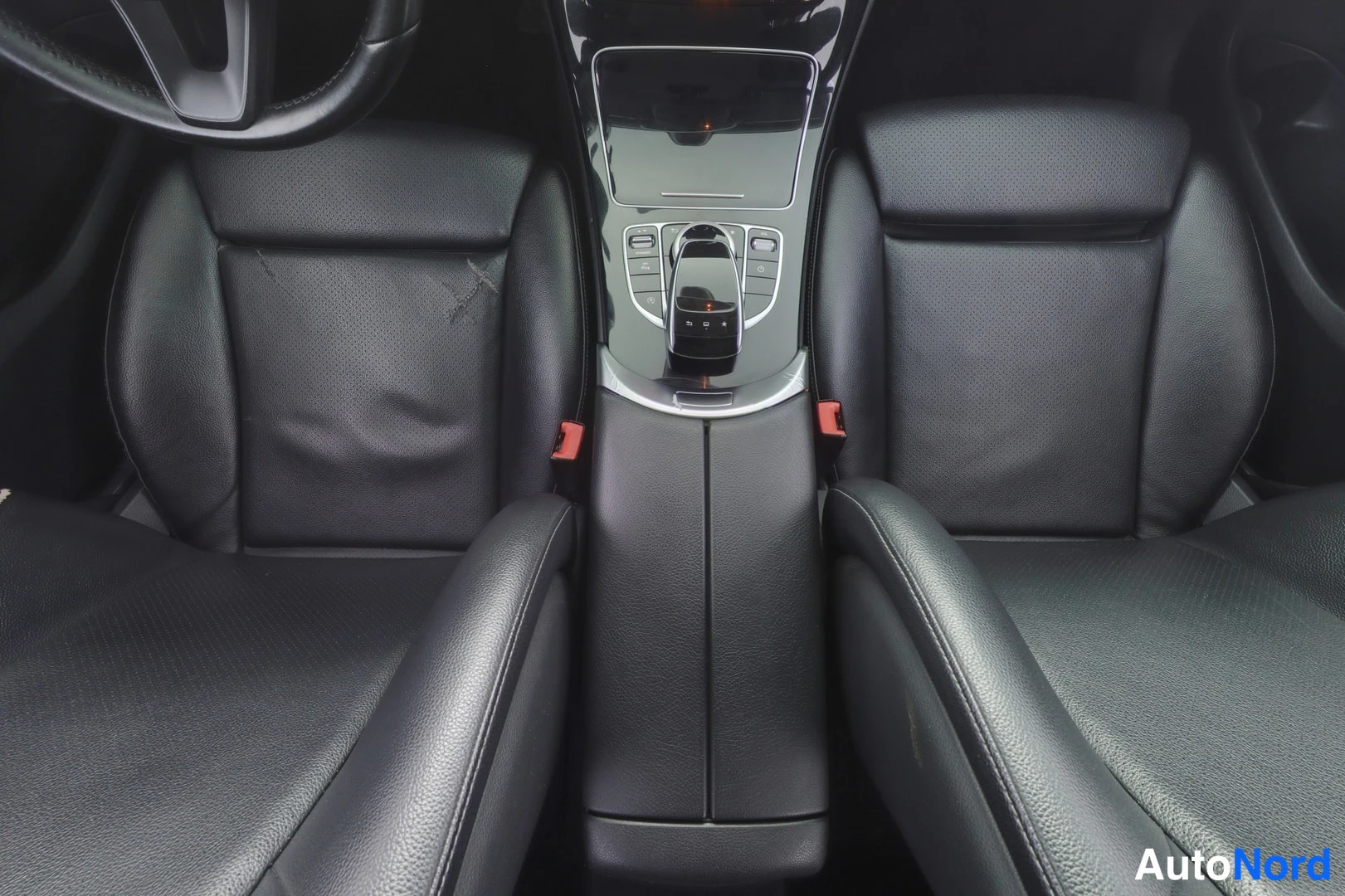 Etuistuimet: Close-up of the front seats in black leather and the central console with a gear selector. The driver's seat shows significant wear and a rip in the side bolste