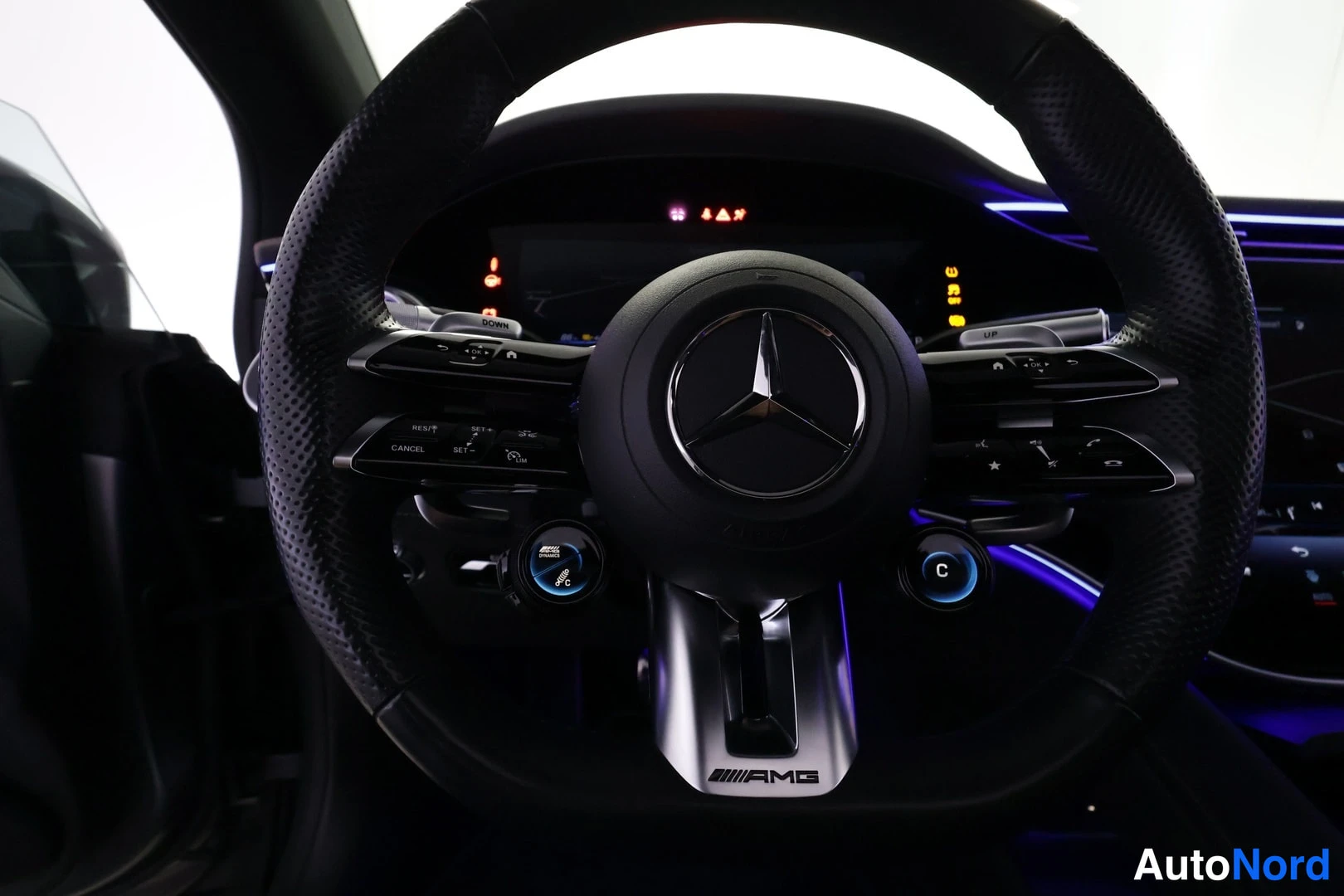 Muu: Sisätilakuva: AMG-ohjauspyörä Mercedes-tähdellä, valuohjaimet, kosketusnauhat ja osa digitaalisesta mittaristosta pimeässä kulmavalaisussa.