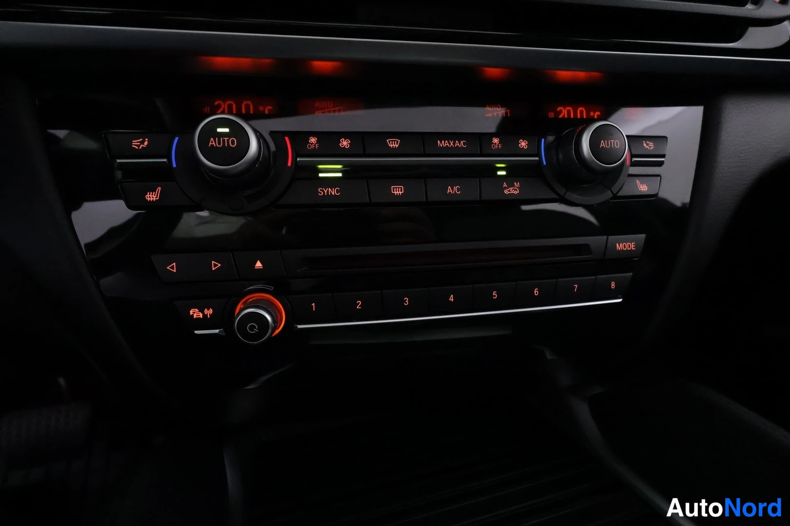 Muu: Auton keskikonsolin ilmastointipaneeli, jossa kaksi AUTO-ruuvikytkintä ja näppäimiä kuten SYNC, A/C ja MAX A/C, lämpötilanäytöt 20,0 °C.