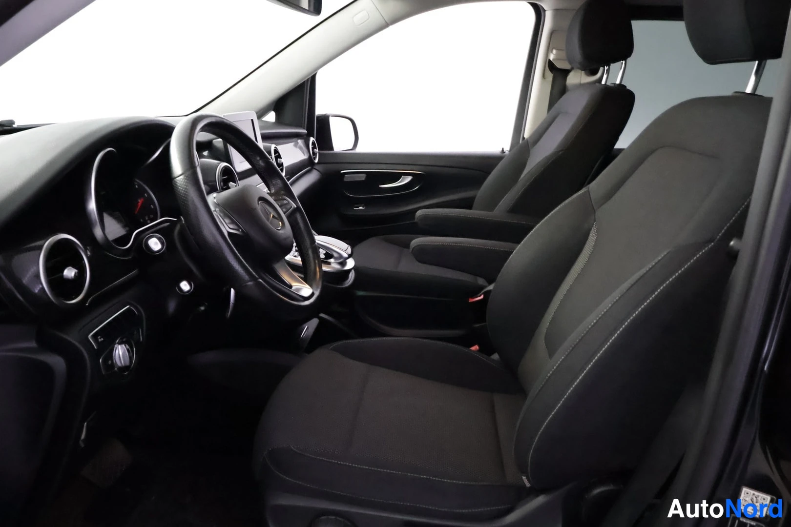 Ohjaamo: Interior view from open door showing front passenger and driver areas. Two captain's chairs in the front row have armrests. Dashboard, steering wheel with logo,