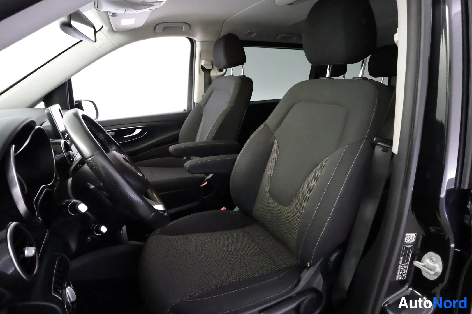 Ohjaamo: Side profile view into the vehicle cabin from the driver side. The front left seat is prominent in the foreground. A second front seat (captain's chair style) i