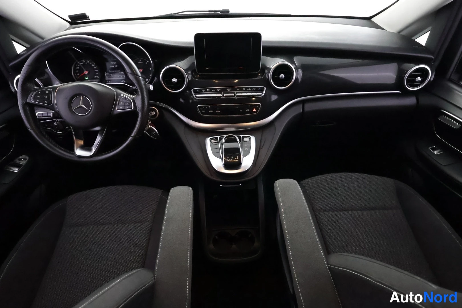 Muu: Mercedes-Benz V:n ohjaamo edestä: Mercedes-merkillä varustettu ratti, mittaristo, keskitörmäessimaalaineen näyttö, ilmastointiaukot ja kaksi tummaa kangasistuin