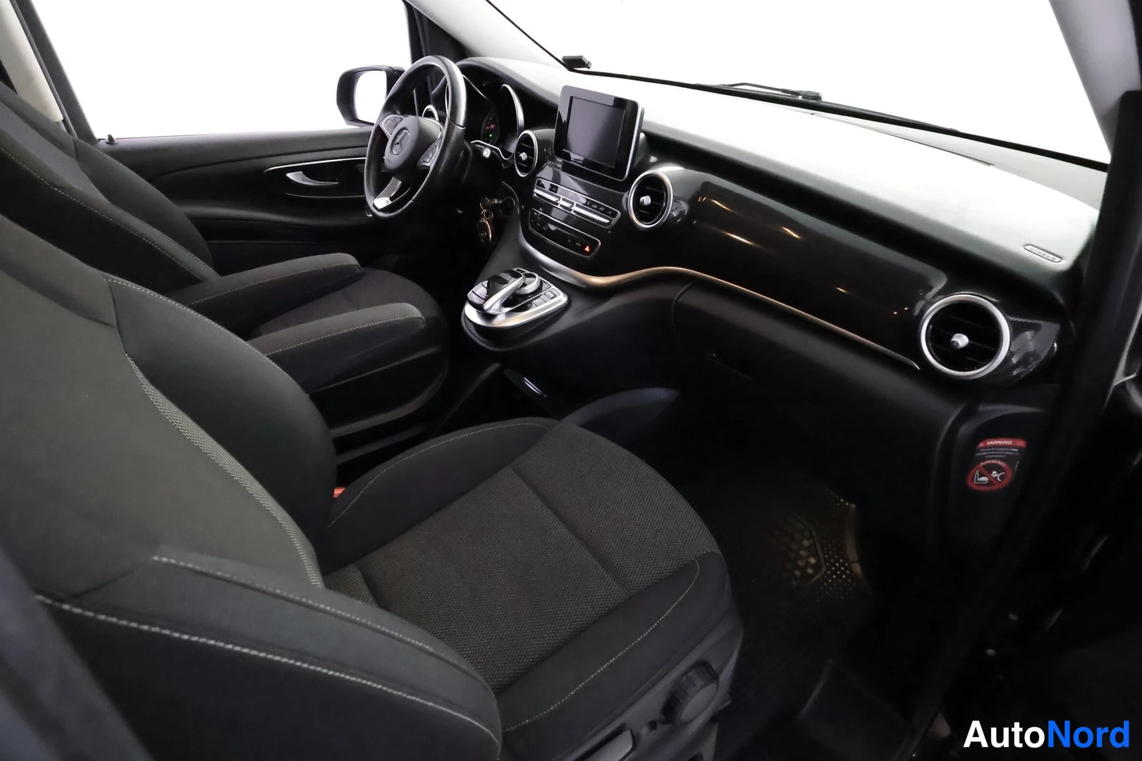 Muu: Mercedes-Benz V:n sisätilat matkustajan puolen ovi auki: kaksi etumaalaista kangasistuinta, tumma kojelauta ja konsolin kahva, lattiassa tumma matto.