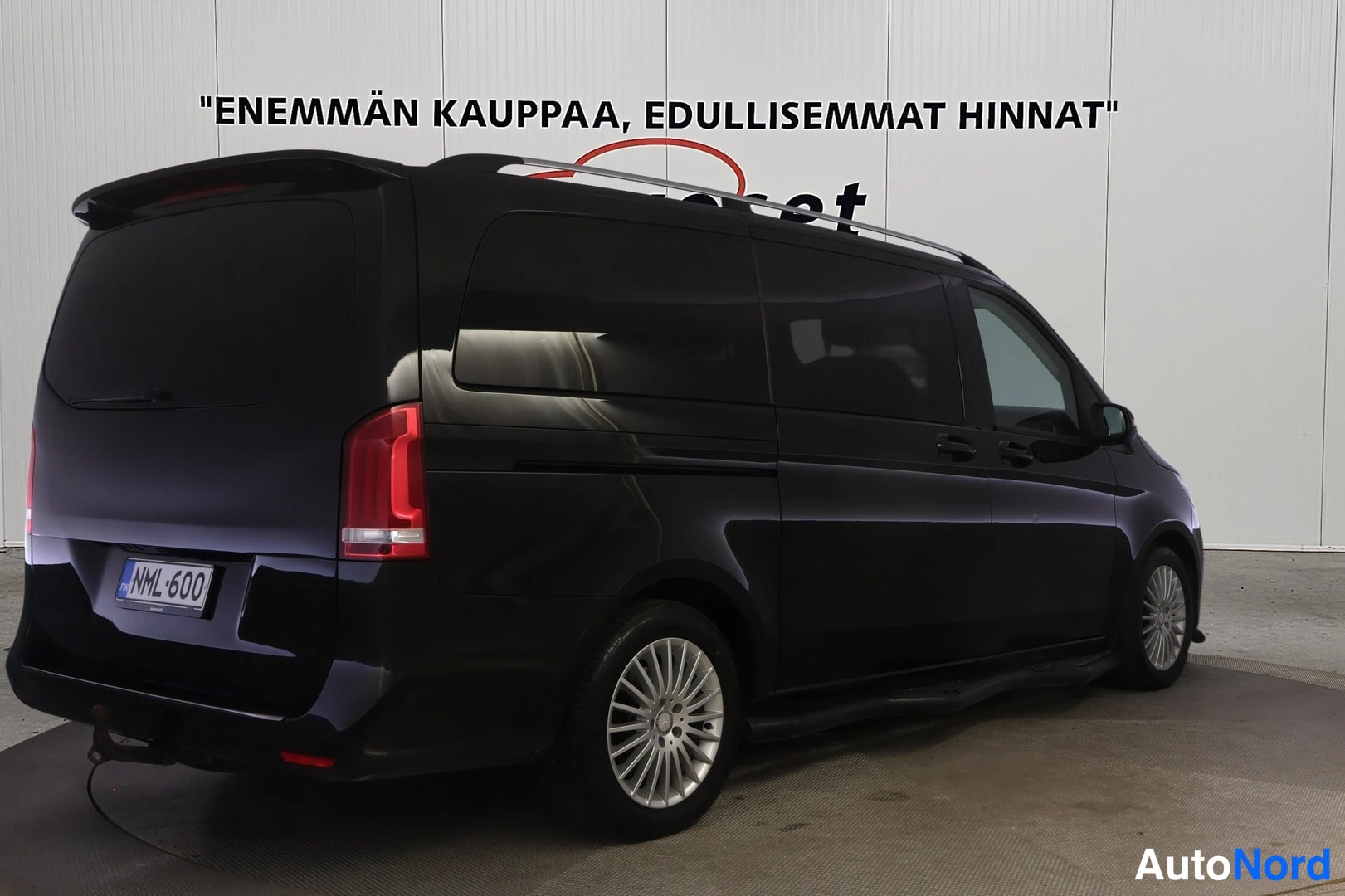 Takaviisto: Musta Mercedes-Benz V -pakettiauto takaa‑sivulta nähtynä, takavalo, rekisterikilpi ja kattokaiteet näkyvät.