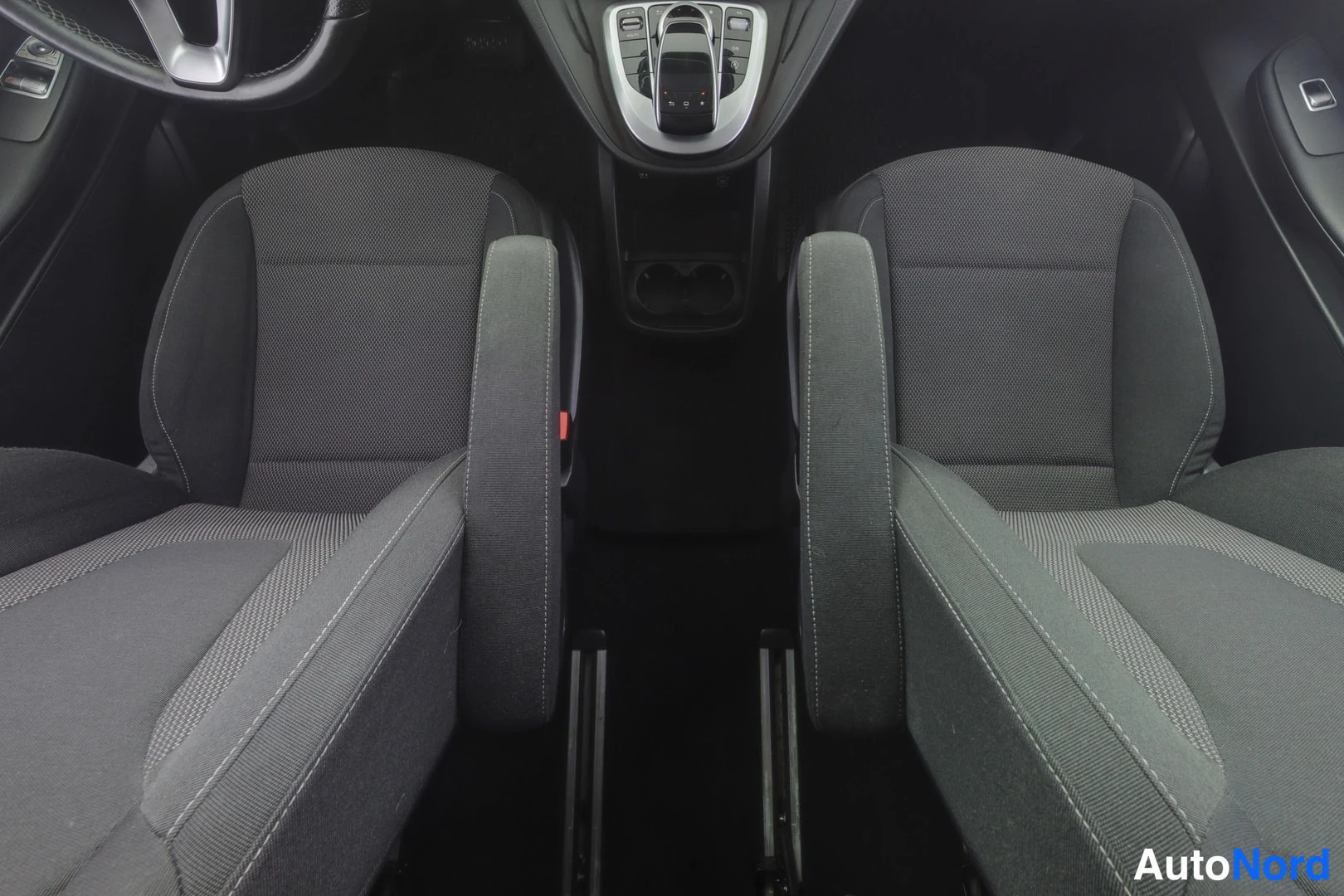 Etuistuimet: View of two front seats with grey fabric upholstery and contrast stitching. Center console, cup holders, and automatic gear selector are visible between the sea