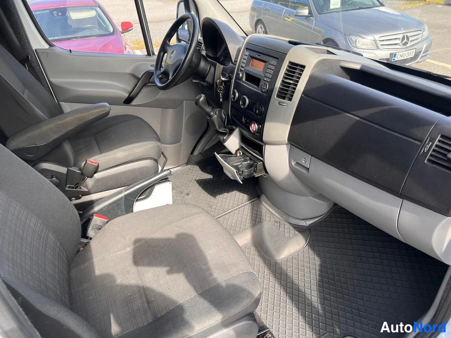 Etuistuimet: Wide shot of the interior showing the driver's seat, left door panel, and the full width of the dashboard and center console. Two front bucket seats with grey f