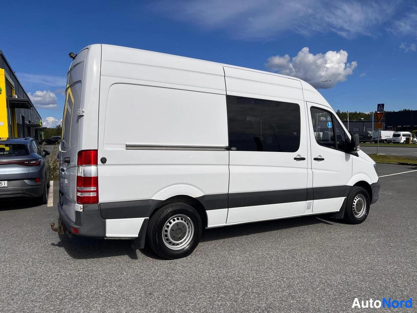 Takaviisto: Mercedes-Benz Sprinter -pakettiauto takavasemmasta kuvattuna, valkoinen korimuovi, tummat alaovet ja savunlasiset takaikkunat.