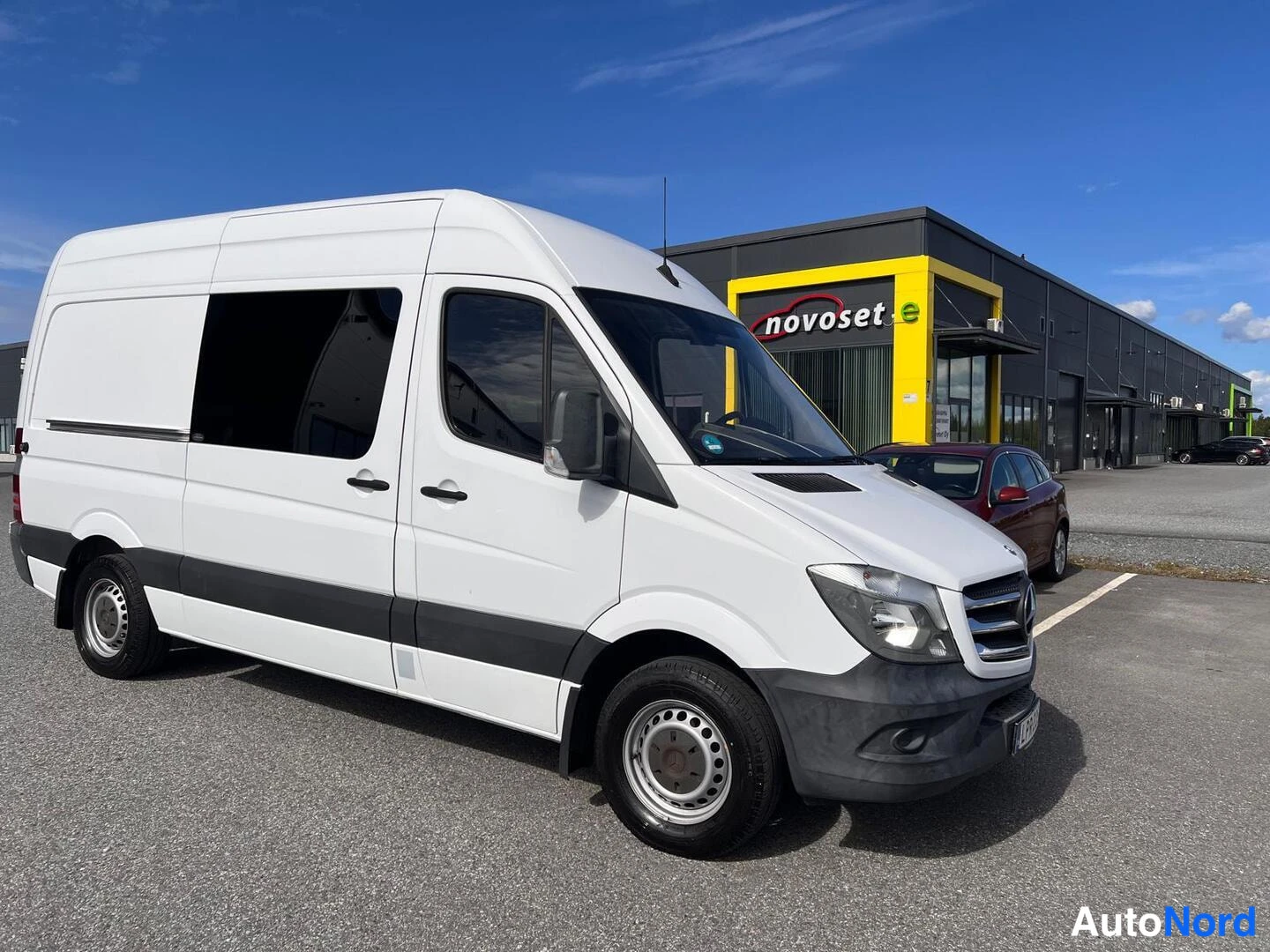 Etuviisto, nokka oikealle: Mercedes-Benz Sprinter -pakettiauto etuoikealta kuvattuna, valkoinen korimuovi, tummat pyöränkaaret ja nokkalokasuoja.