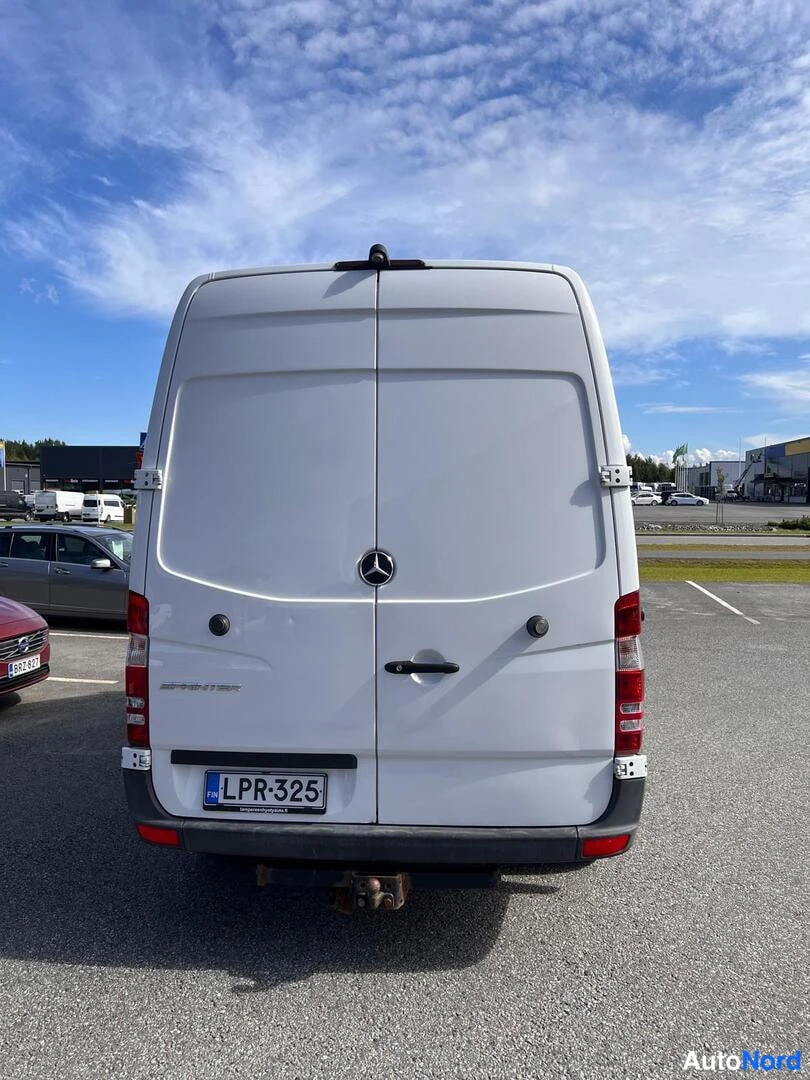 Takaa: Takana kuvattu valkoinen pakettiauto. Takaluukussa Mercedes-merkki ja rekisterikilpi. Taustalla taivaan pilviä.
