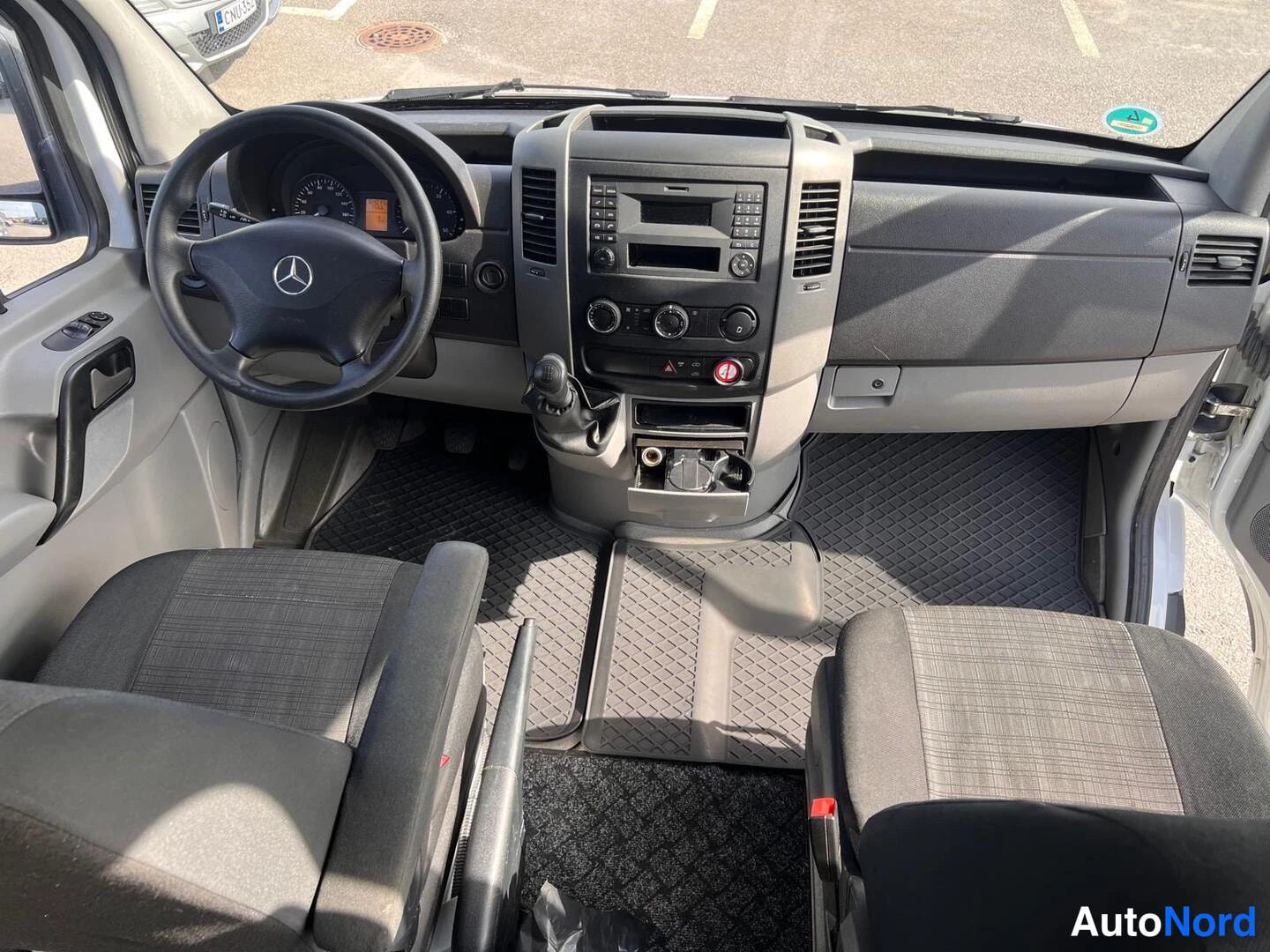 Etuistuimet: Cockpit view of the driver's area showing the steering wheel, dashboard controls, central console with a radio and climate control unit. The front cabin feature
