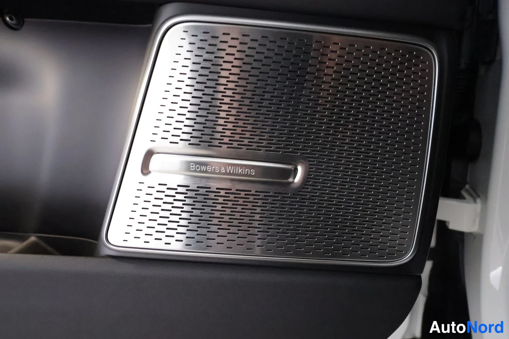 Muu: Auton sisätilan detalji: harmaa perforoitu metallikaiutinritilä, jossa lukee kaiverrettuna ”Bowers & Wilkins”.