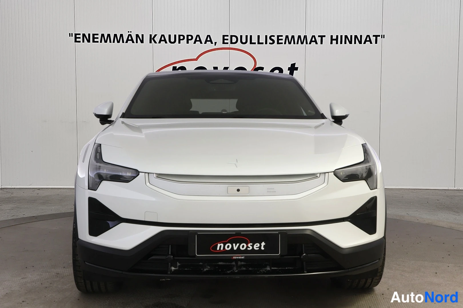Edestä: Valkoisen Polestar 3:n suora etunäkymä: ajovalot, suljettu etugrilli ja novoset-tekstillä varustettu etulokasuoja.