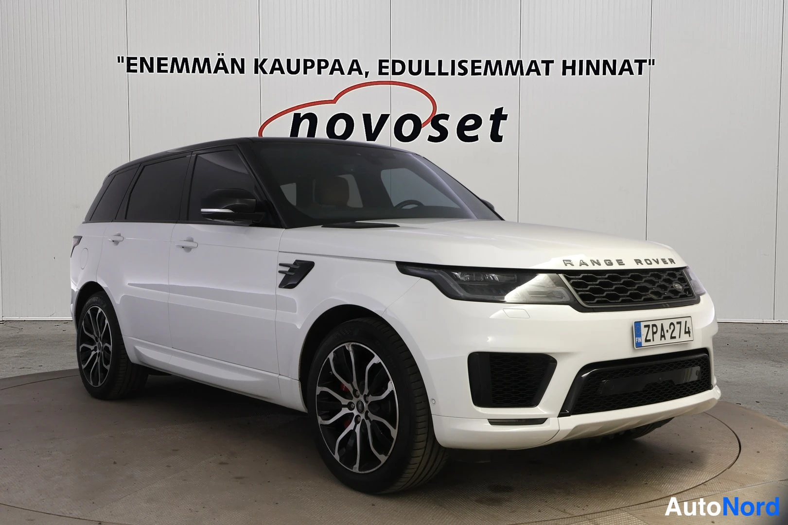 Etuviisto, nokka oikealle: Valkoinen Land Rover Range Rover Sport, etusivu kolmessa neljäsosassa, musta katto ja mustat kevytmetallivanteet, rekisteritunnus.