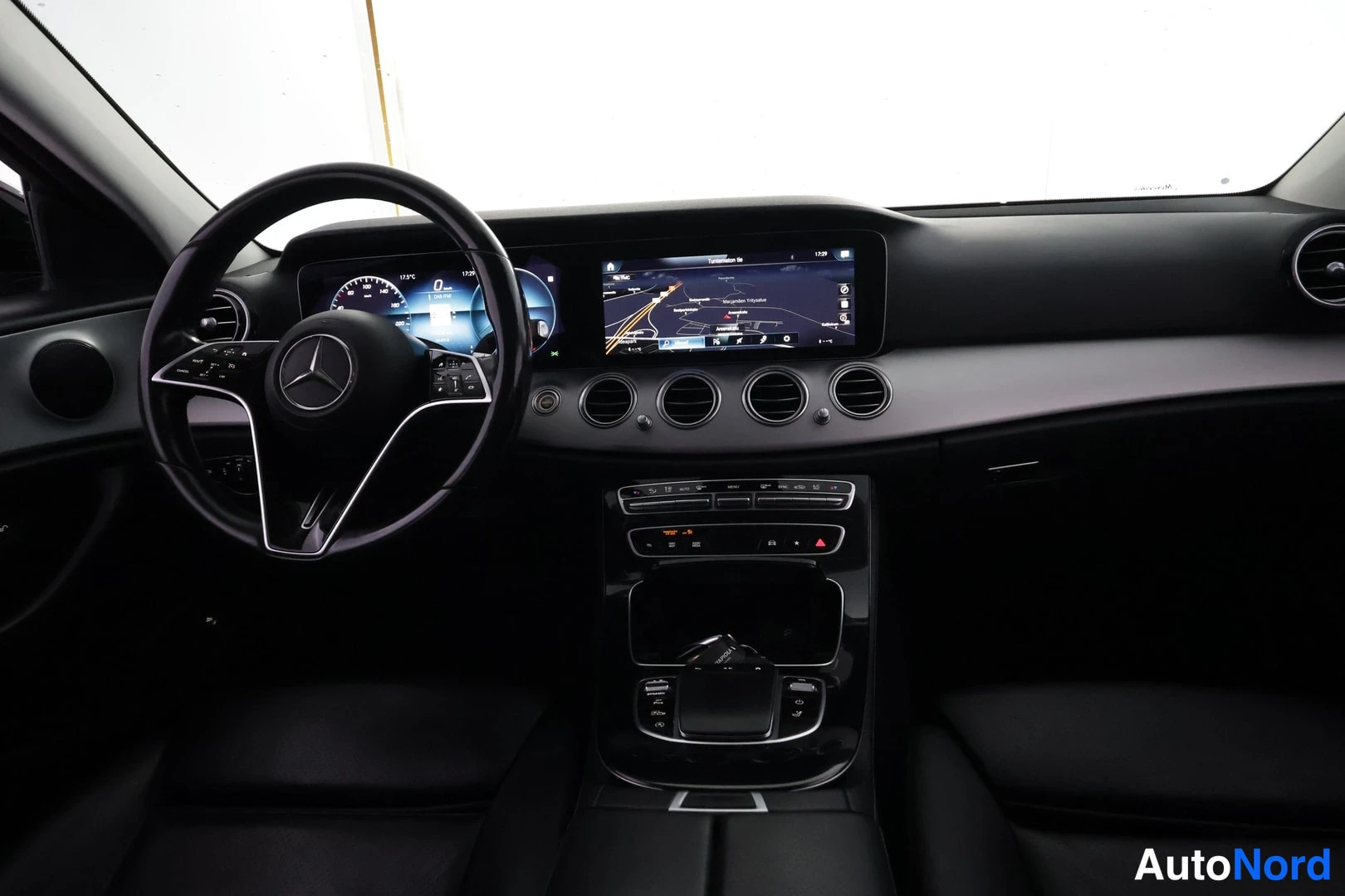 Edestä: Ohjaamo edestä kuvattuna: Mercedes-Benzin ohjauspyörä, digitaalinen mittaristo ja laaja vaakasuuntainen infotainment-näyttö, jossa on karttaohjaus.