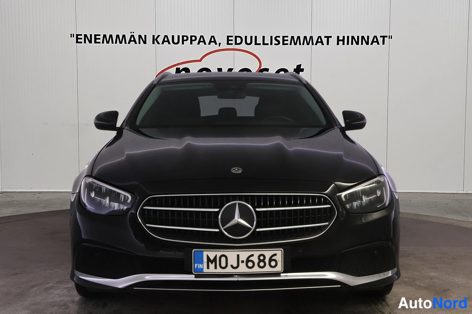 Edestä: Musta Mercedes-Benz E-mallin farmariauto edestä kuvattuna. Grilli, ajovaloissa oleva LED-valo ja rekisterikilpi 'M0J-686' näkyvät.