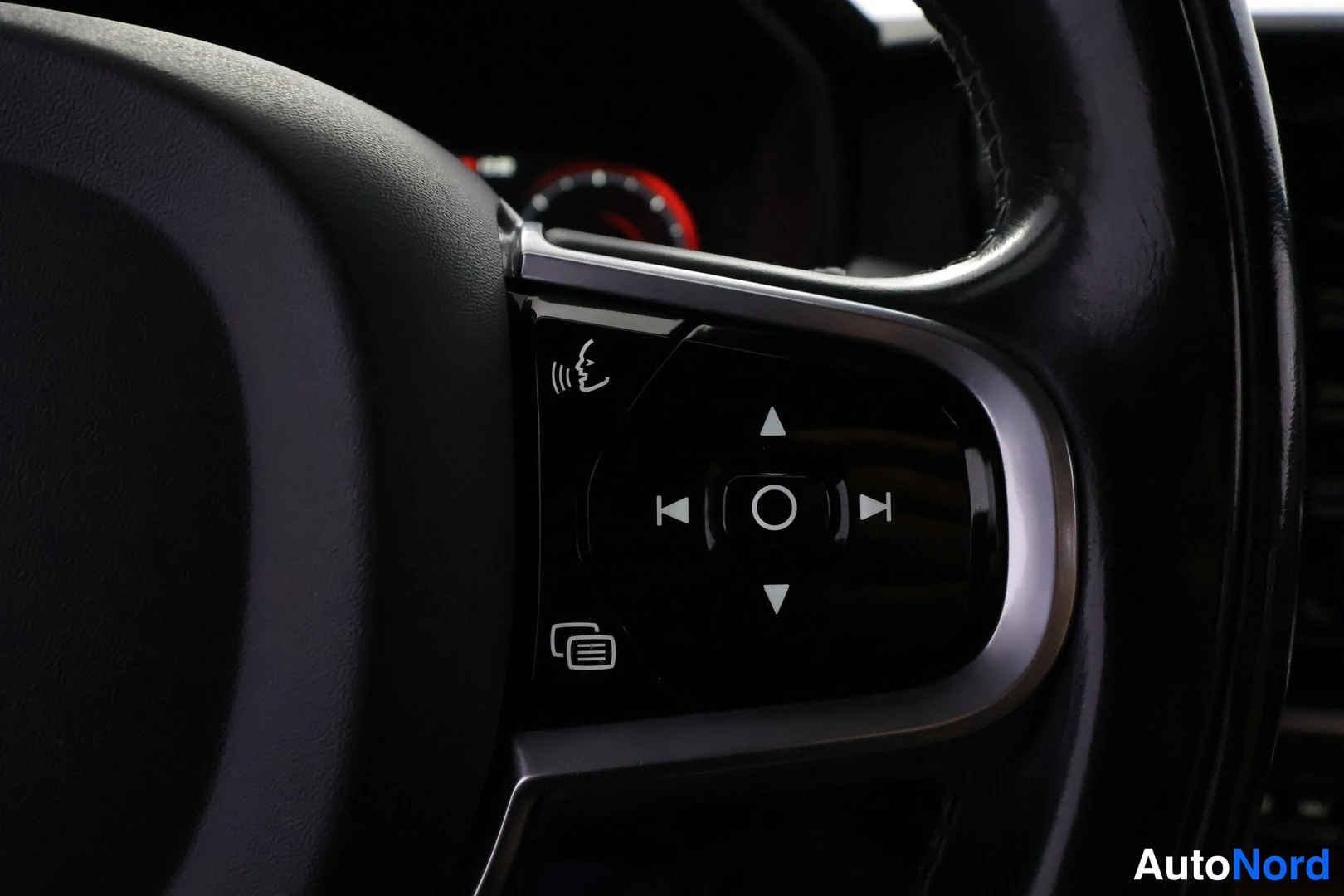 Yksityiskohta: Volvo S90 Inscription 2017 – kuvan 1: ratti, lähikuva. Rattirivin nappien kuvat: ratti, navigointi- ja ääniohjausnappi.