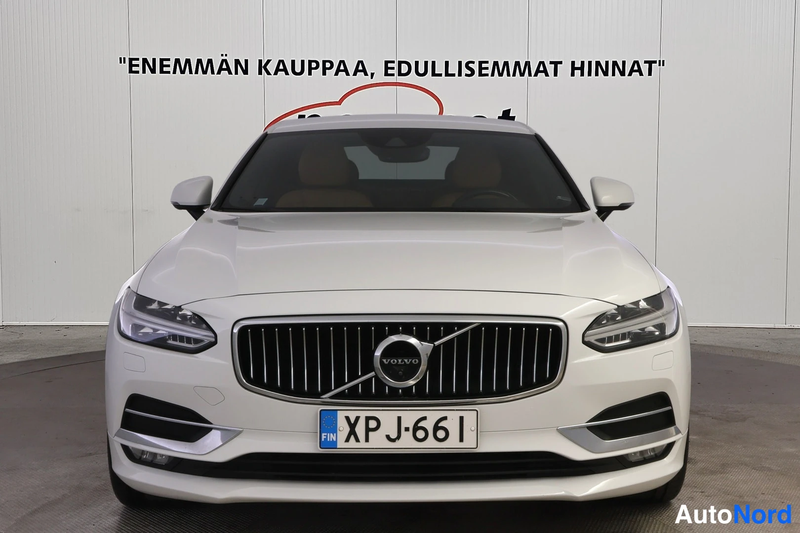 Edestä: Valkoisen sedanin suora etunäkymä: pystysäleikköinen keulagrilii VOLVO-merkki, LED-ajovalot ja SINI-keltainen rekisteri.