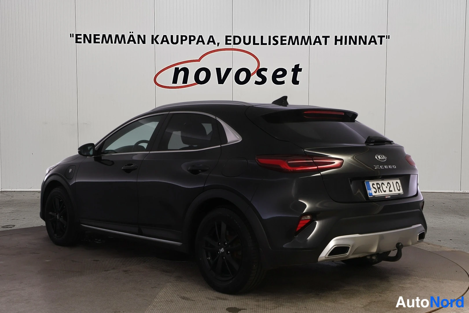 Takaviisto: Kia XCeed, musta farmuri kuvattu takaviistolta, valkoinen novoset-tausta.