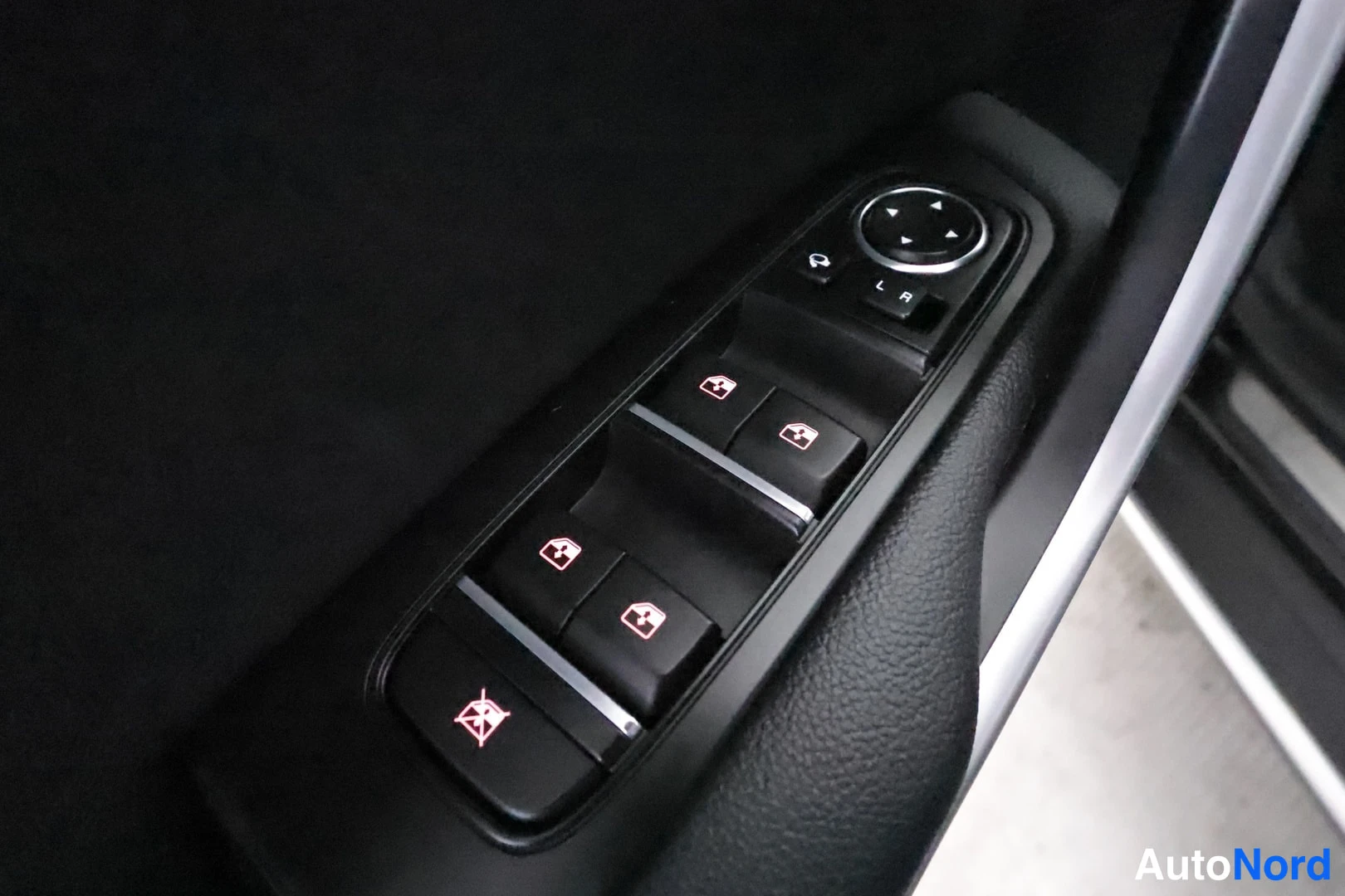 Yksityiskohta: A close-up angled view of a black car door control panel showing buttons for four electric windows and mirror adjustments on a textured surface.