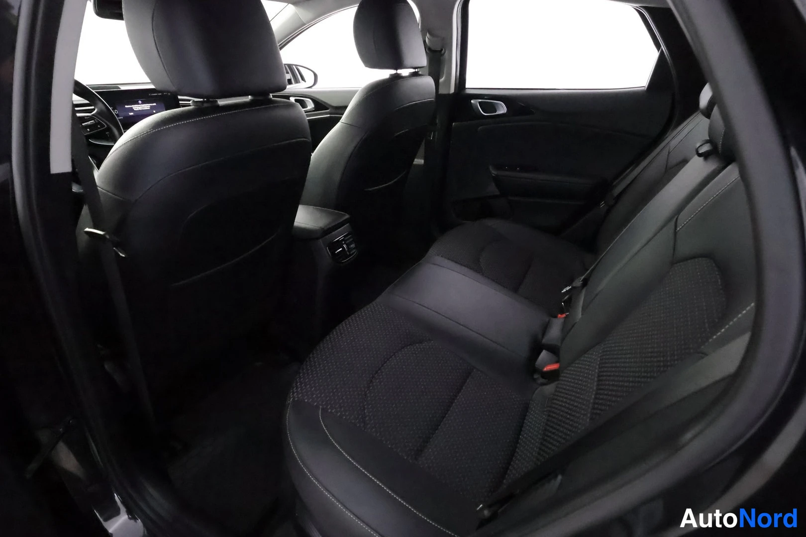 Takaistuimet: The rear passenger compartment viewed from the side shows two rows of black seats with white stitching. ISOFIX anchor points are visible on the outer seat cushi