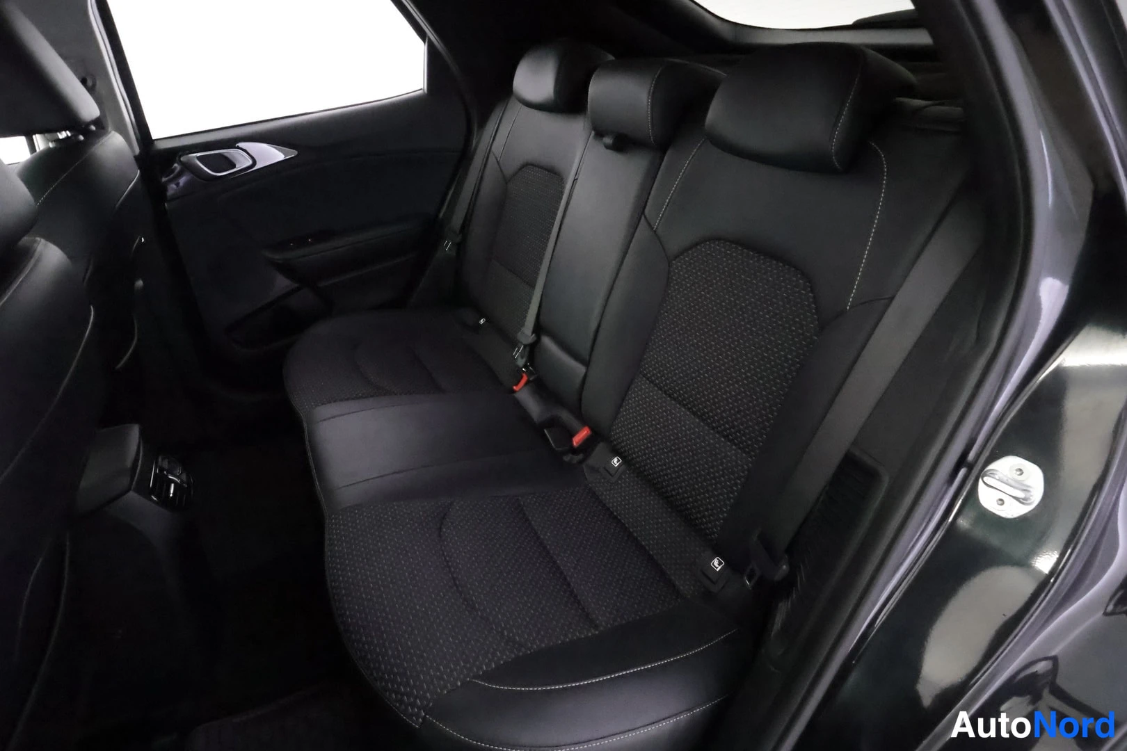 Takaistuimet: A detailed view of the black rear bench seat highlights a perforated central fabric section framed by smooth materials and white topstitching.