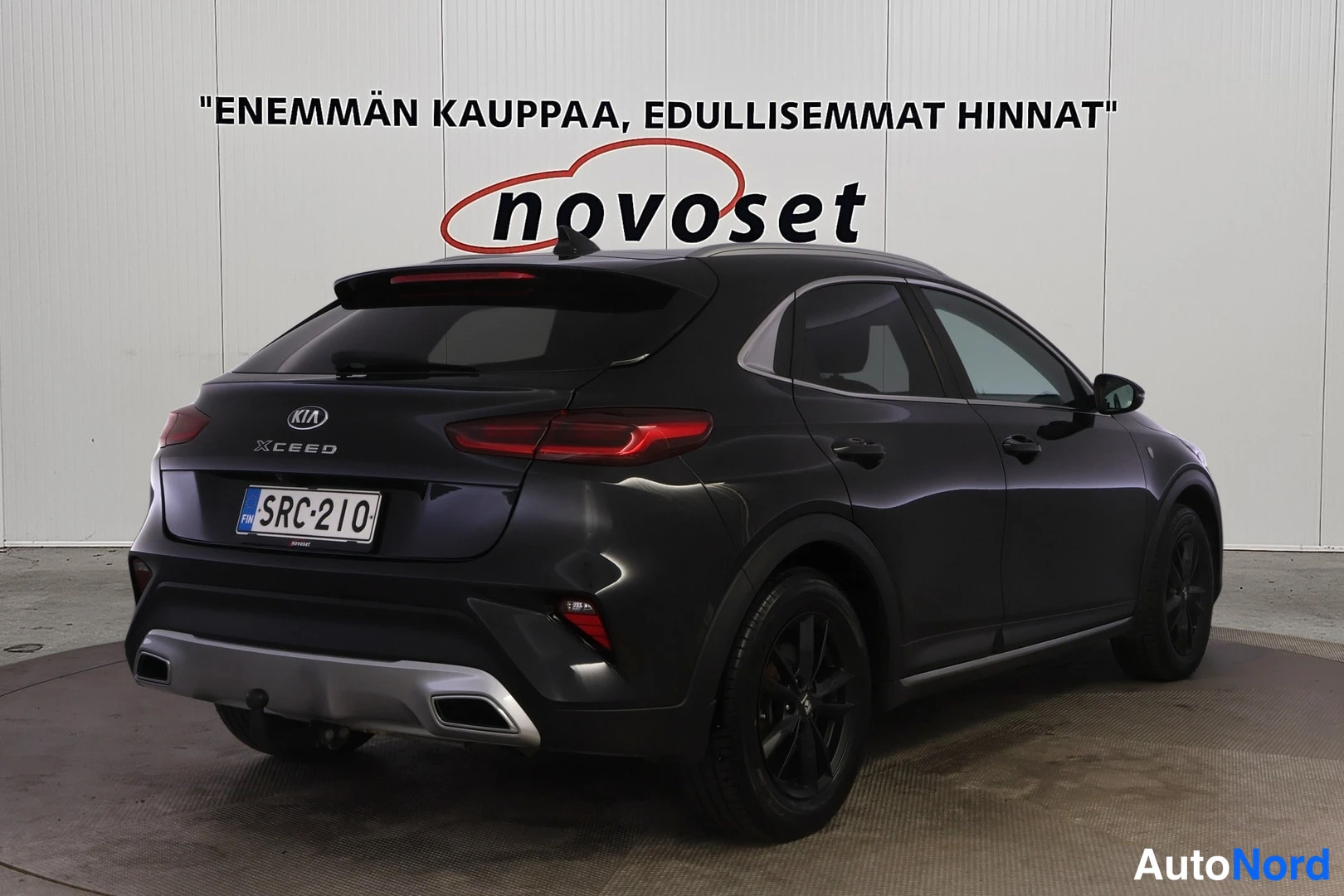 Takaviisto: Kia XCeed, musta farmuri kuvattu takaviistolta oikealta, valkoinen novoset-tausta.