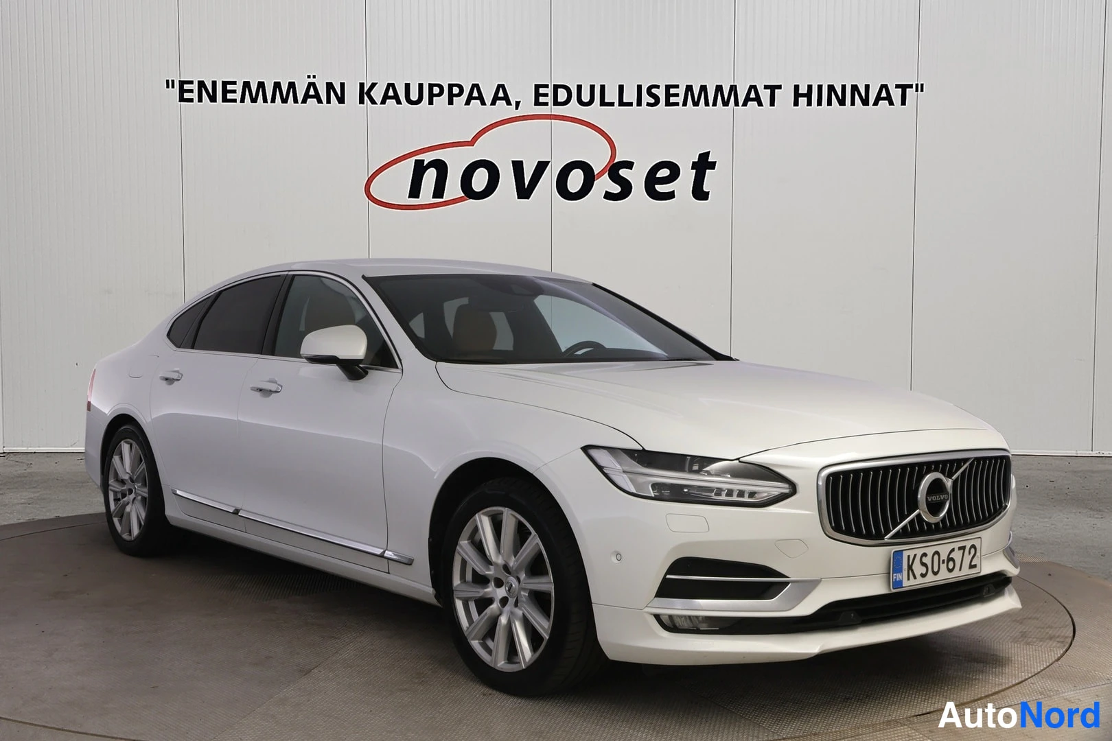 Etuviisto, nokka oikealle: Valkoinen Volvo S90 -lihavatuva kolmionkulma kuva, jossa etuosa ja vasen sivu ovat näkyvissä. Alumiinivanteet, LED-päiväturvat ja kromikoristeet ovenkynn