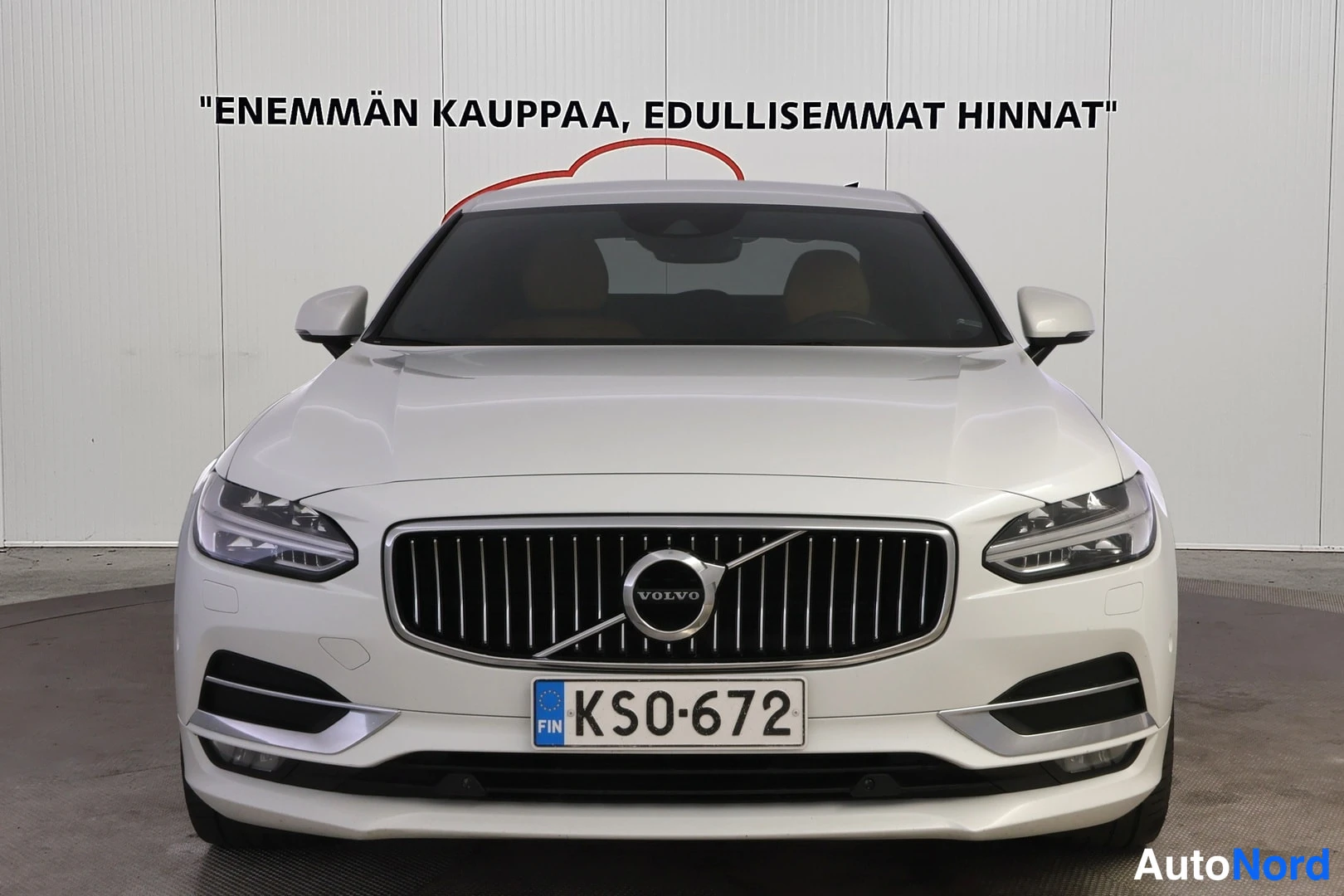 Edestä: Suora etukuva valkoisesta Volvo S90:stä. Grilli, Volvo-logon merkki, LED-valot ja rekisterikilpi KS0-672.