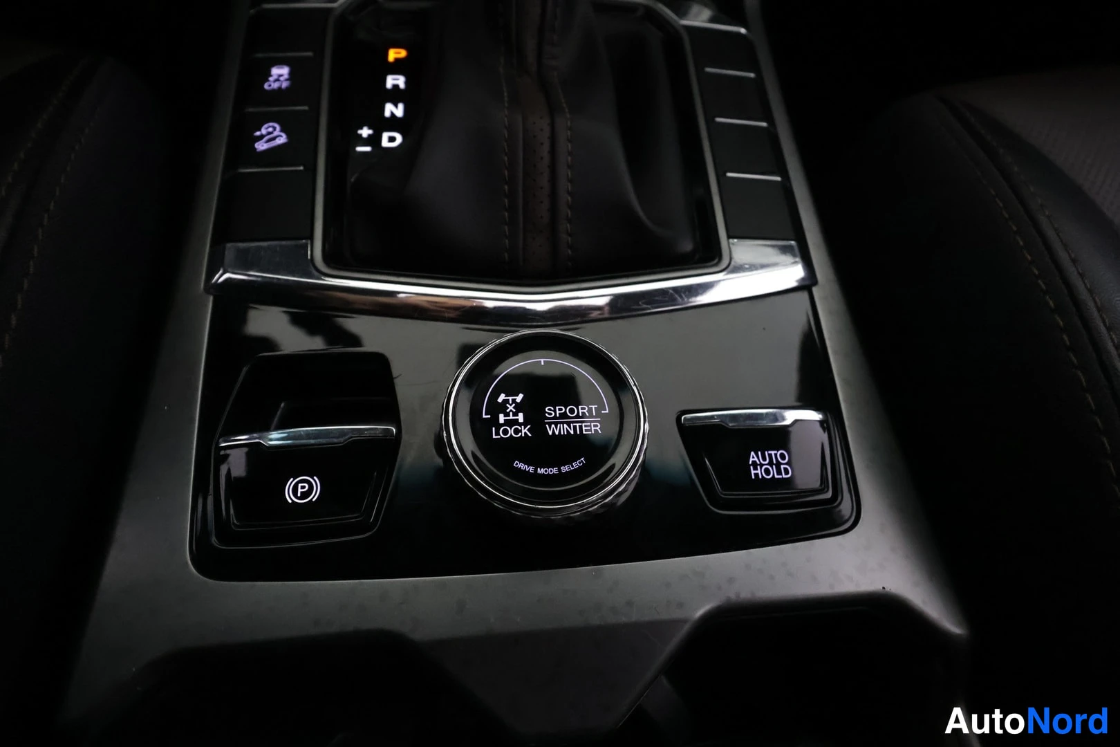 Ohjaamo: Kuvassa keskuspaneelin lähikuva, jossa vaihteiston ympärillä on kytkimiä kuten AUTO HOLD ja SPORT MODE SELECT -painike.