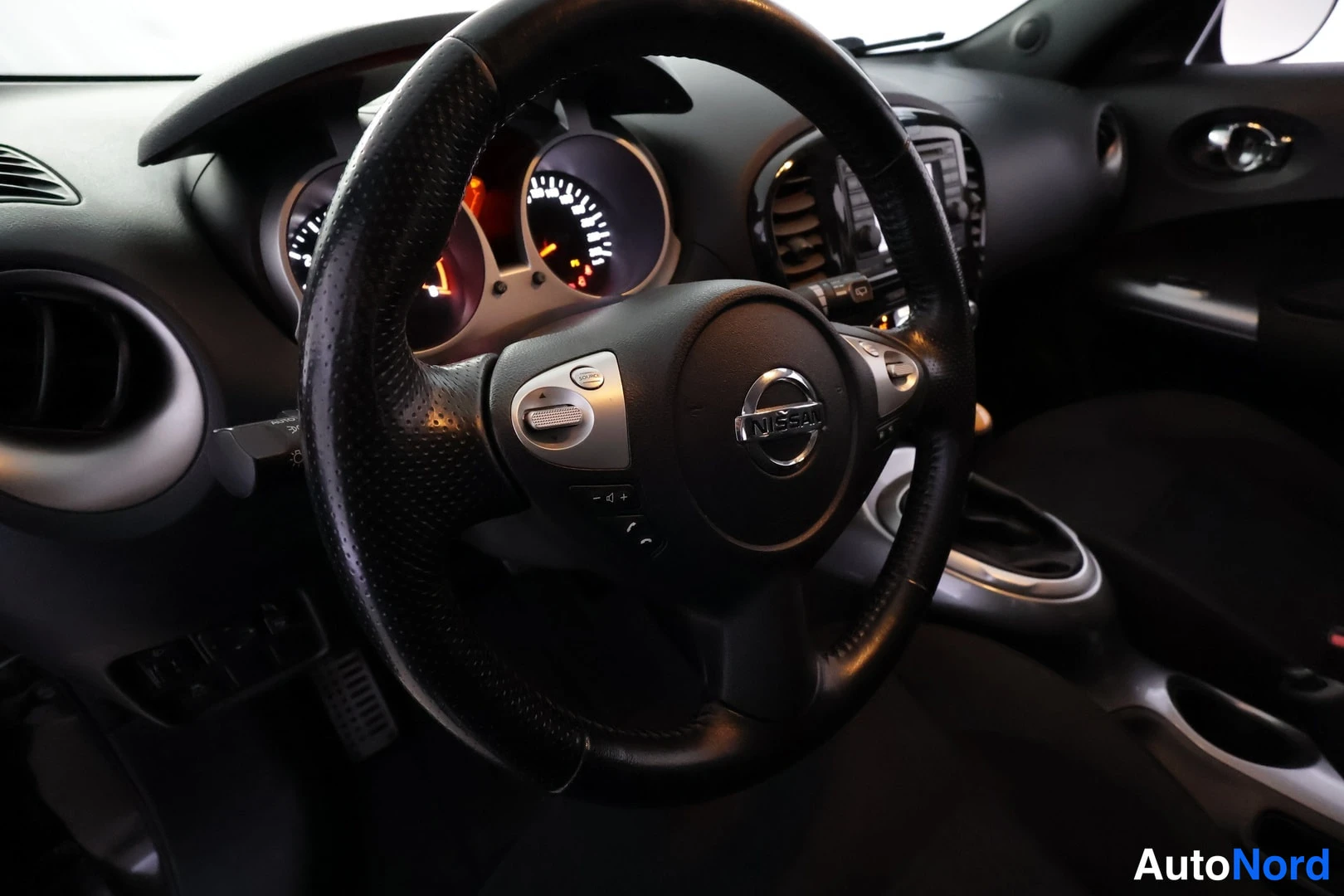 Etuviisto: Ohjauspyörä lähikuvassa Nissan-logolla, mittaristo ja kojelauta sekä vaihdekepin ympäristö taustalla.