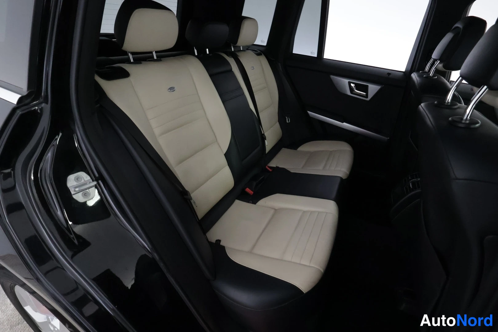Yksityiskohta: Mercedes-Benzin takapenkki vasemmasta takavöstä kuvattuna; beige-mustat nahkapenkit, päänokat ja takioven saranat näkyvät.