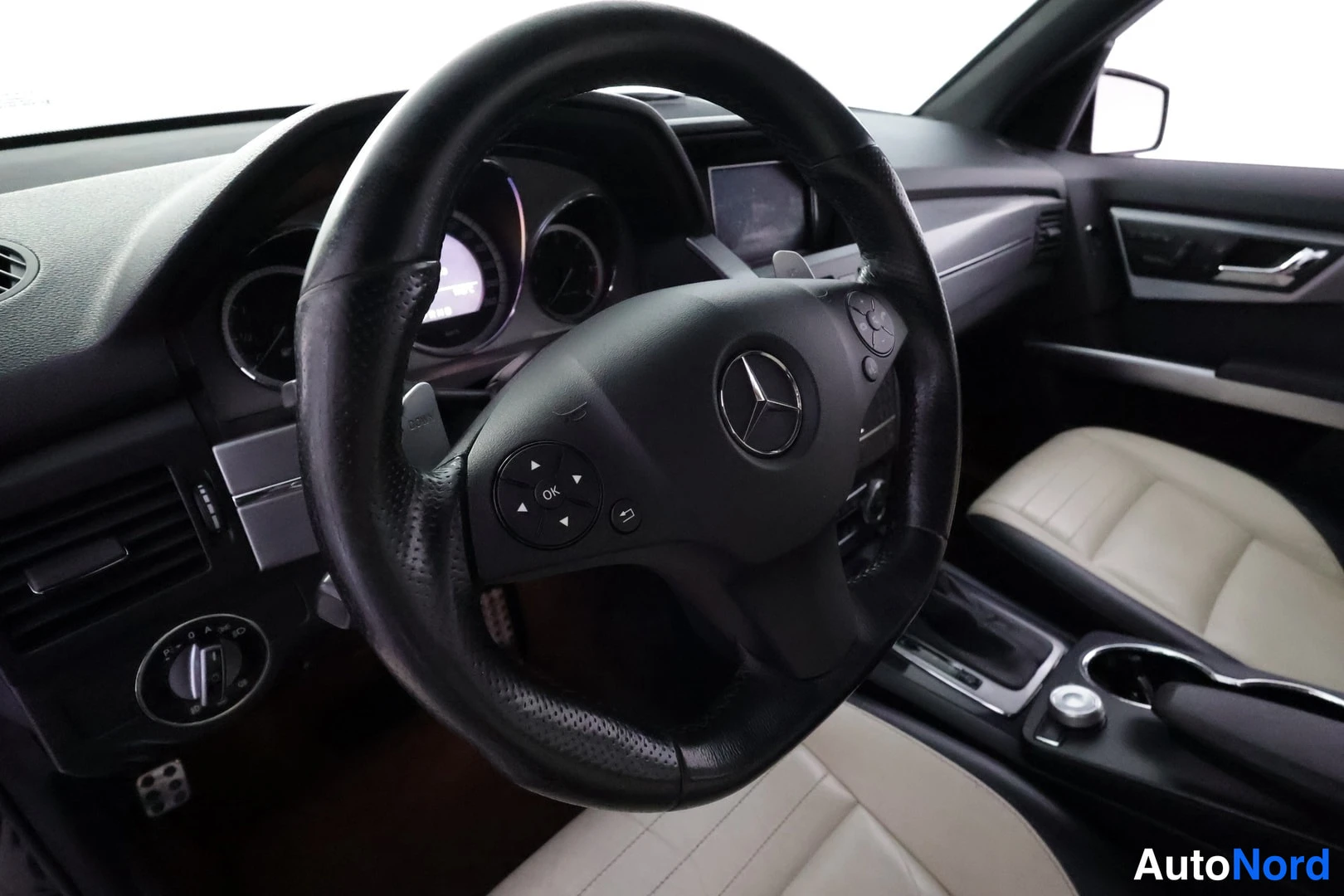 Muu: Ohjauspyörä ja kojelauta sisältä; Mercedes-tähti ohjauspyörän keskellä, beige-mustat nahkaistuimet ja tumma mittaristo näkyvissä.