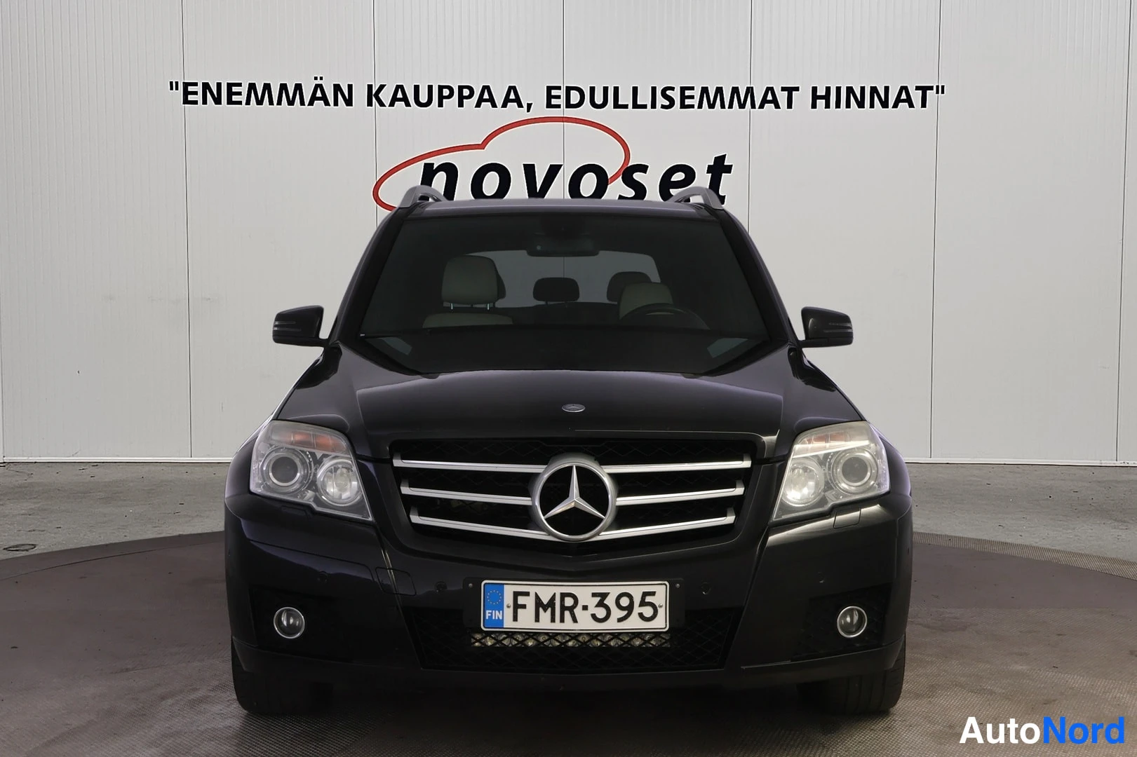 Edestä: Mustan Mercedes-Benzin etupää suoraan edestä: keskellä Mercedes-tähti säleikössä, sumuvalot molemmin puolin ja rekisterilabel.