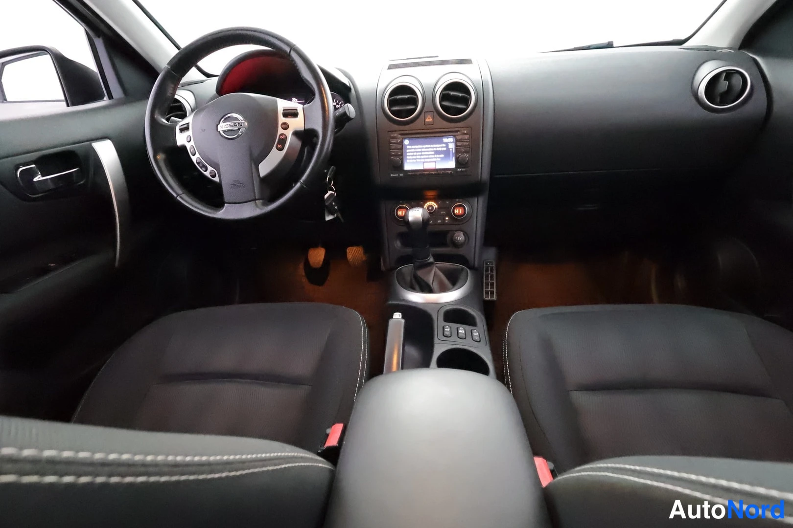 Edestä: Ohjaamo etupästä: Nissan-ohjauspyörä, manuaalivaihteiston kahva, keskikonsolin radio ja ilmastointinapit, kaksi etuistuinta.