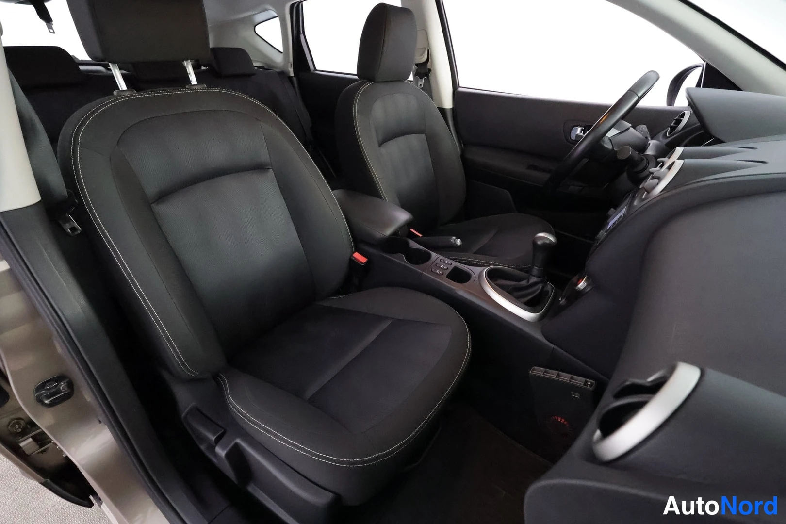 Edestä: Nissanin sisätilat: mustat kankaan etuistuimet ja keskihonka, vaihdekeppi ja ratti kuvassa oikealla.